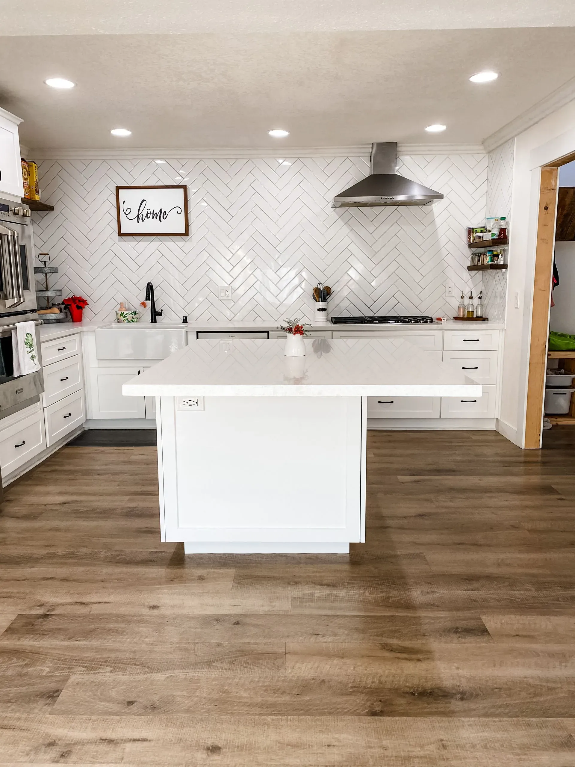 Bright modern kitchen with white cabinets, central island, herringbone backsplash, and wood floors