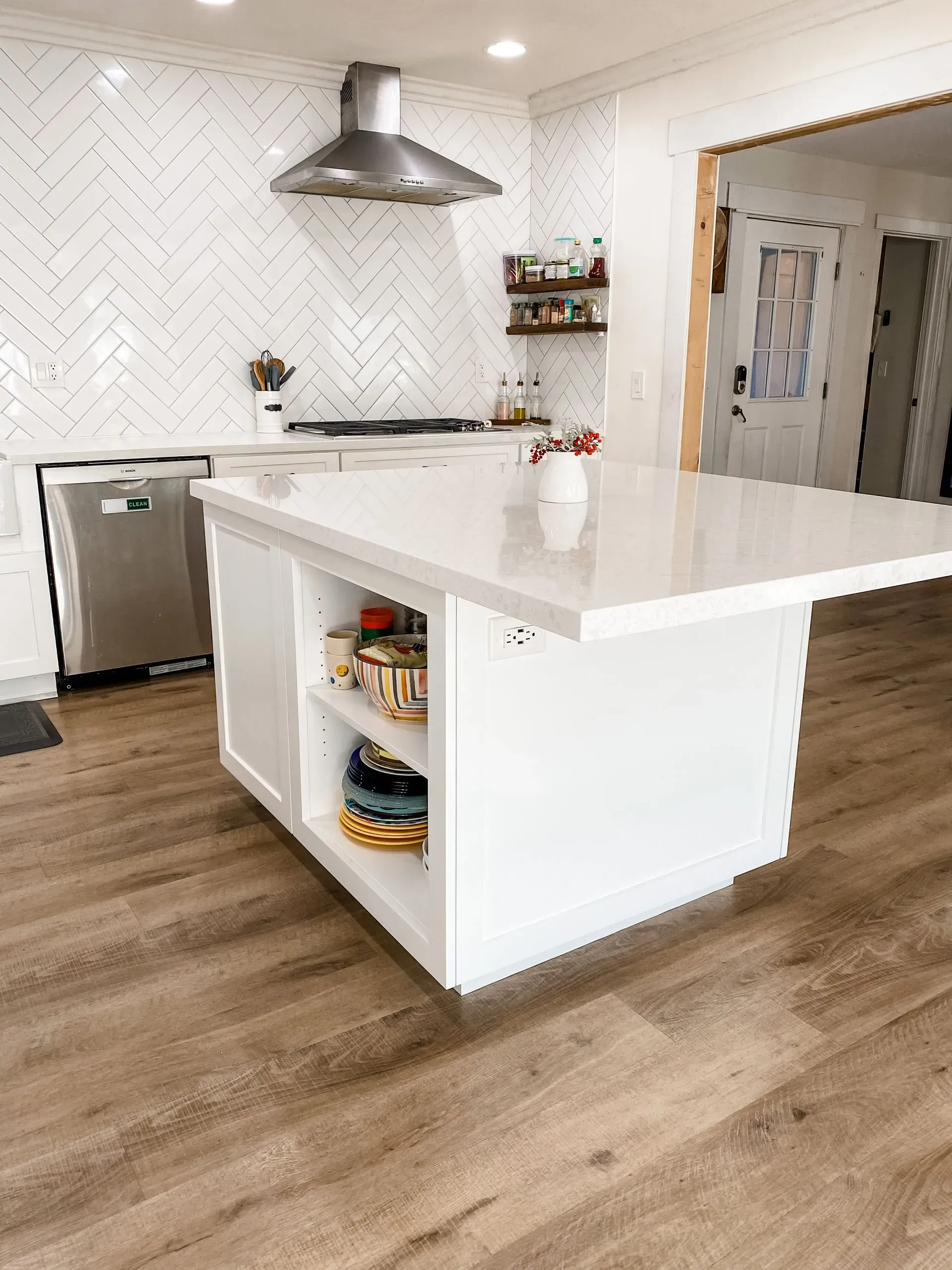 Modern kitchen with white island, stainless steel range hood, and wood-look flooring
