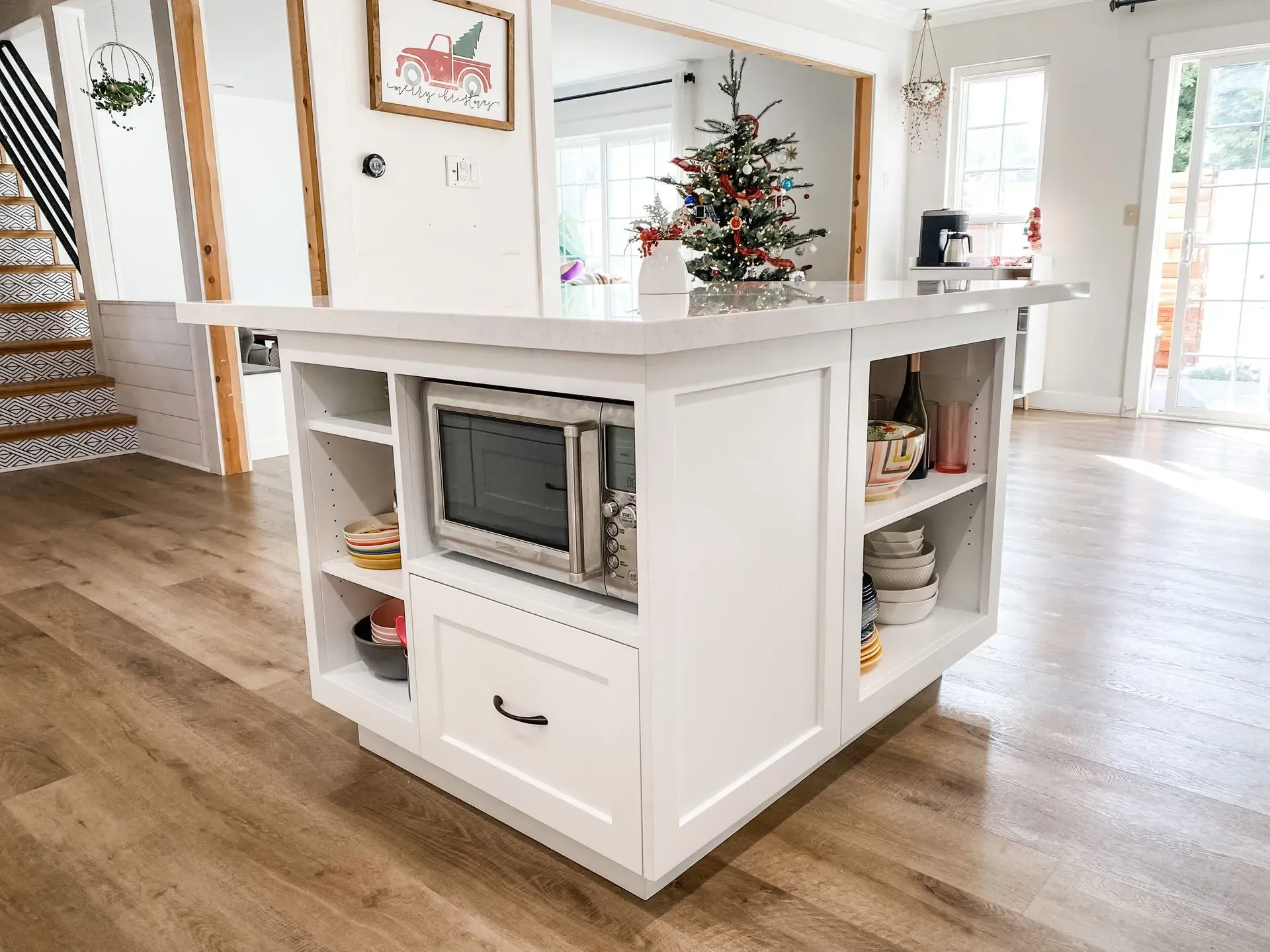 White kitchen island with built-in microwave and drawer, in a bright open-plan home with a Christmas tree nearby