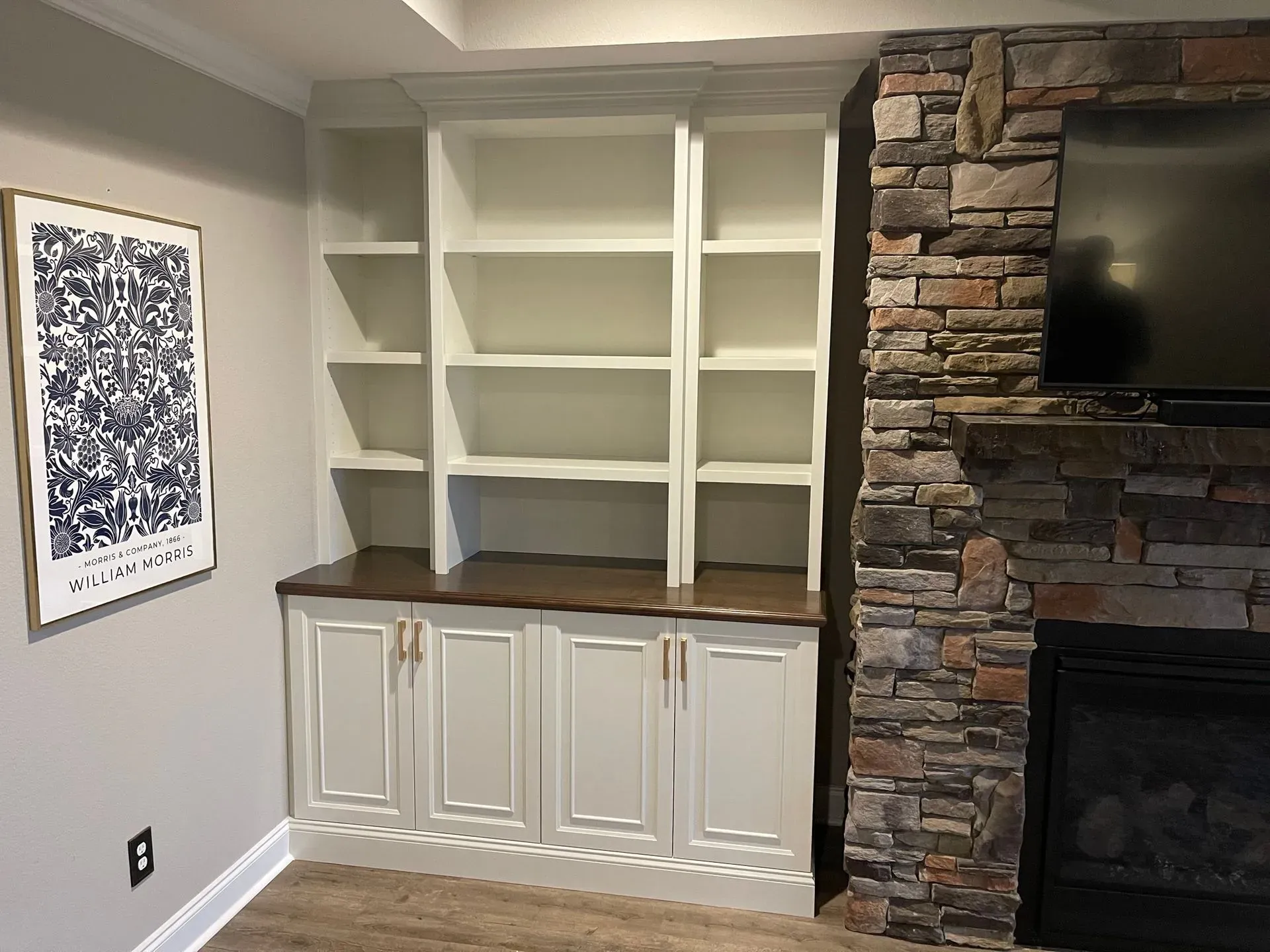Built-in white shelves and cabinets beside a stone fireplace in a living room.