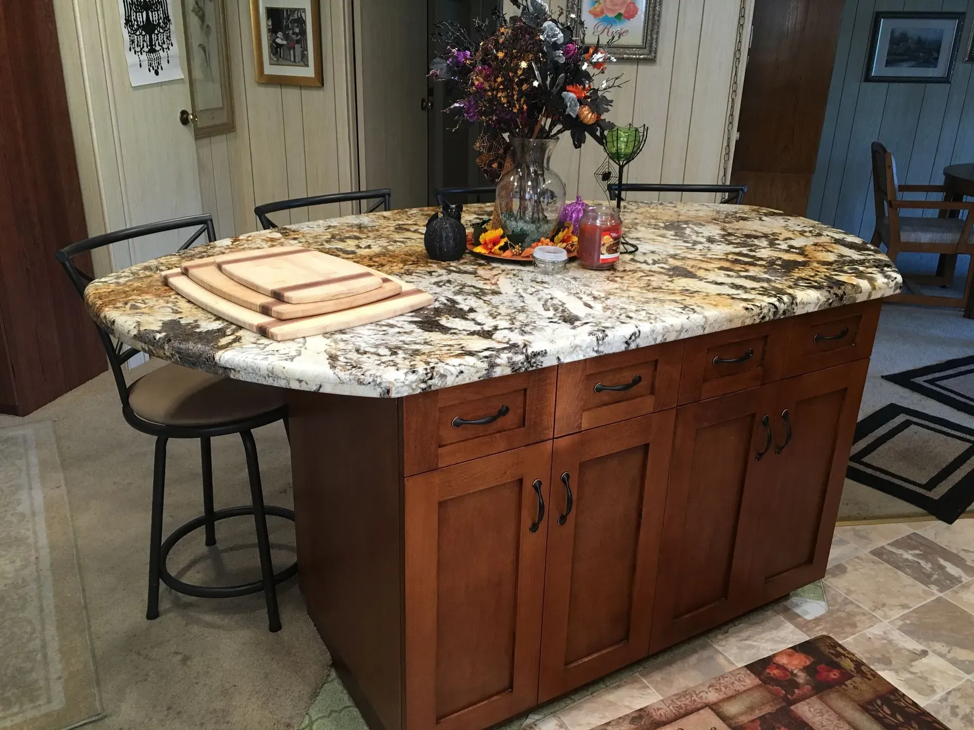 Kitchen island with granite countertop, wooden cabinets, and stools in a warmly lit home interior.