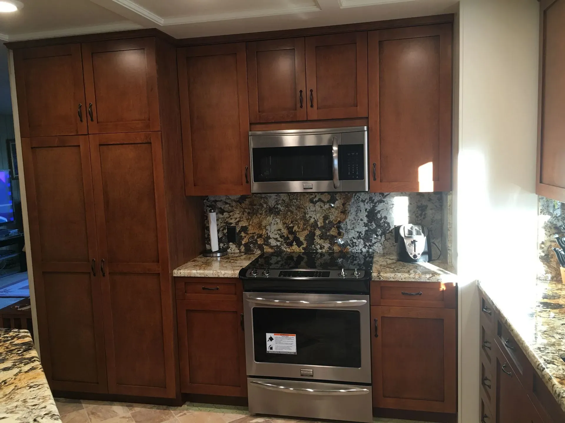 Kitchen with dark wood cabinets, stainless steel oven and microwave, granite countertops, and bright window light