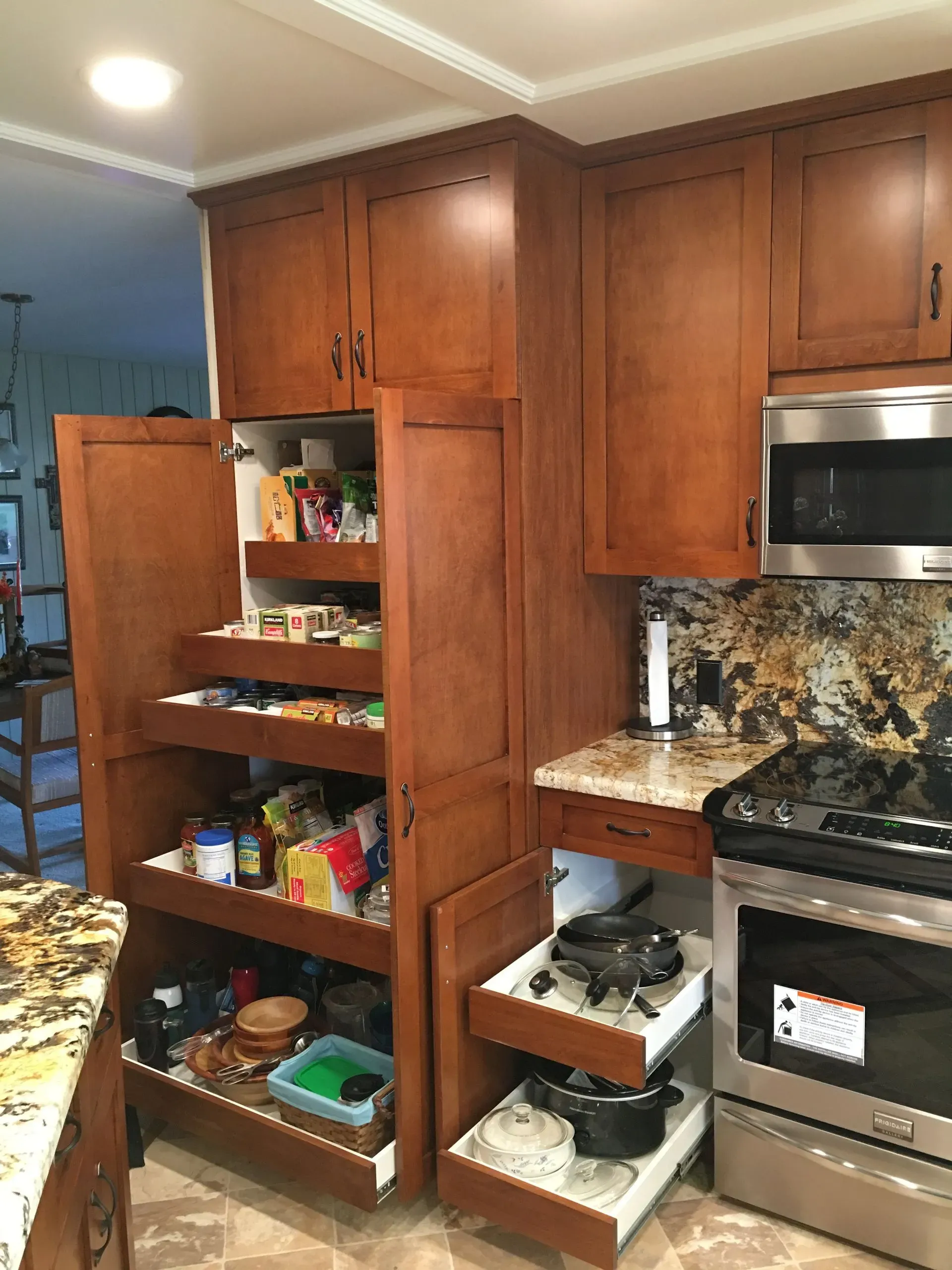 Kitchen with open pantry cabinets, stocked shelves, and stainless steel oven beside a granite countertop.