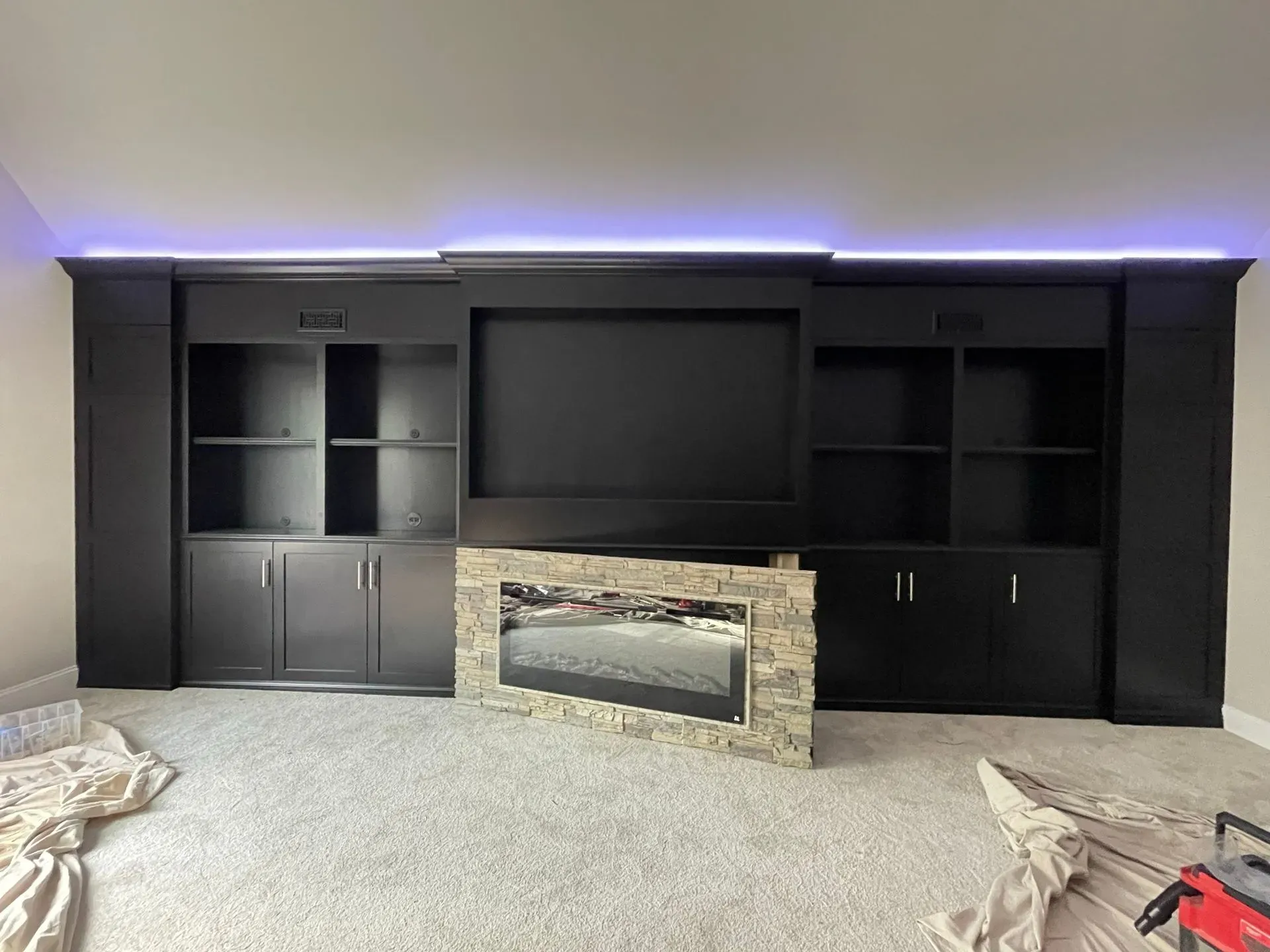 Dark built-in entertainment center with stone fireplace and purple LED lighting in a living room.