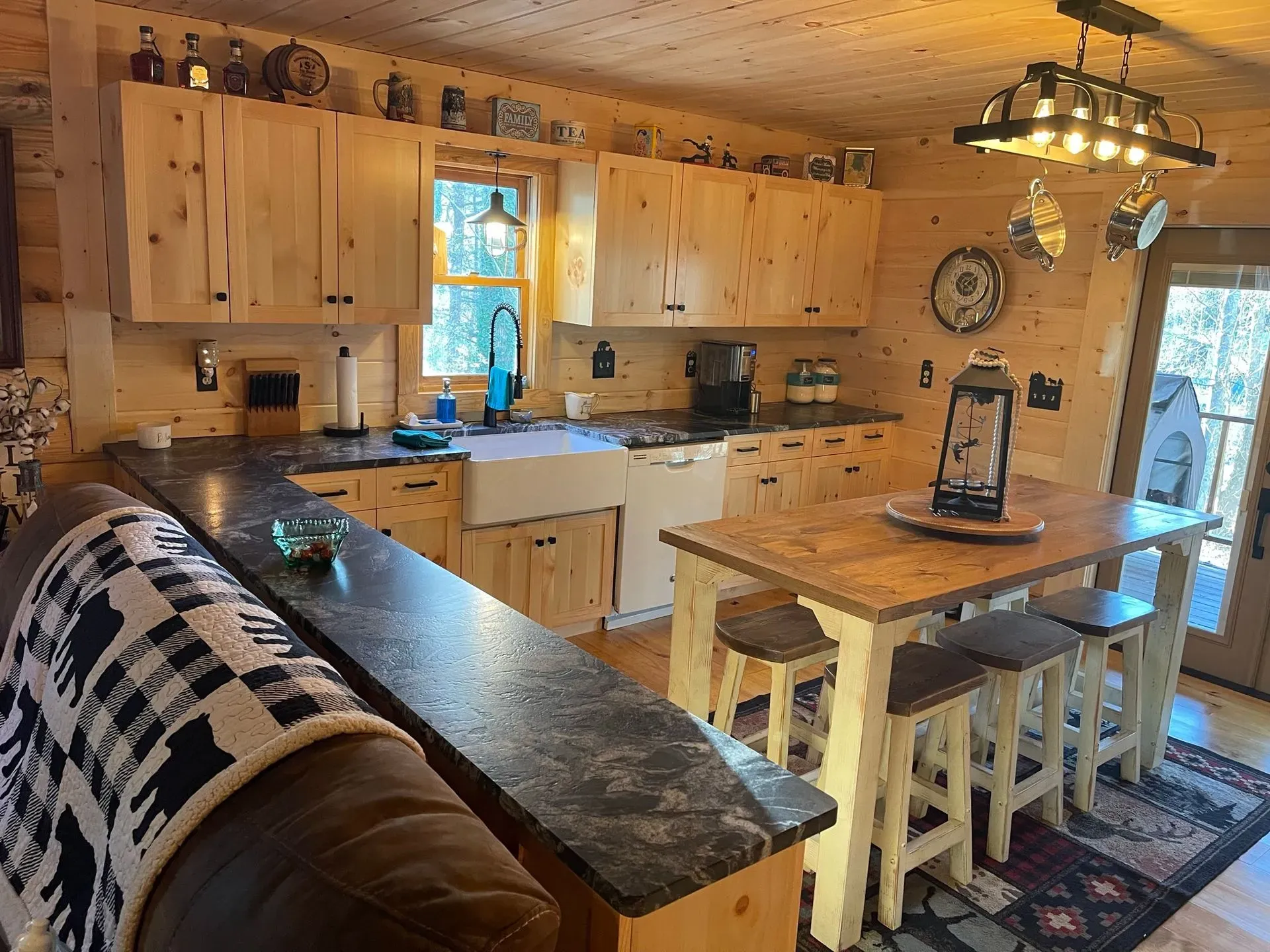 Warm wooden kitchen with island, white cabinets, black countertops, and a dining table by a window and door.