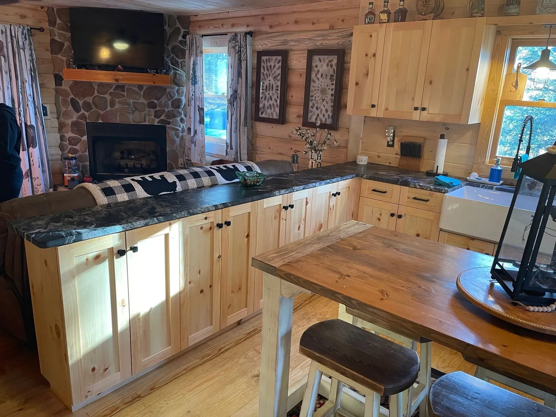 Cozy rustic kitchen with wood cabinets, black countertops, stone fireplace, and dining table by the window