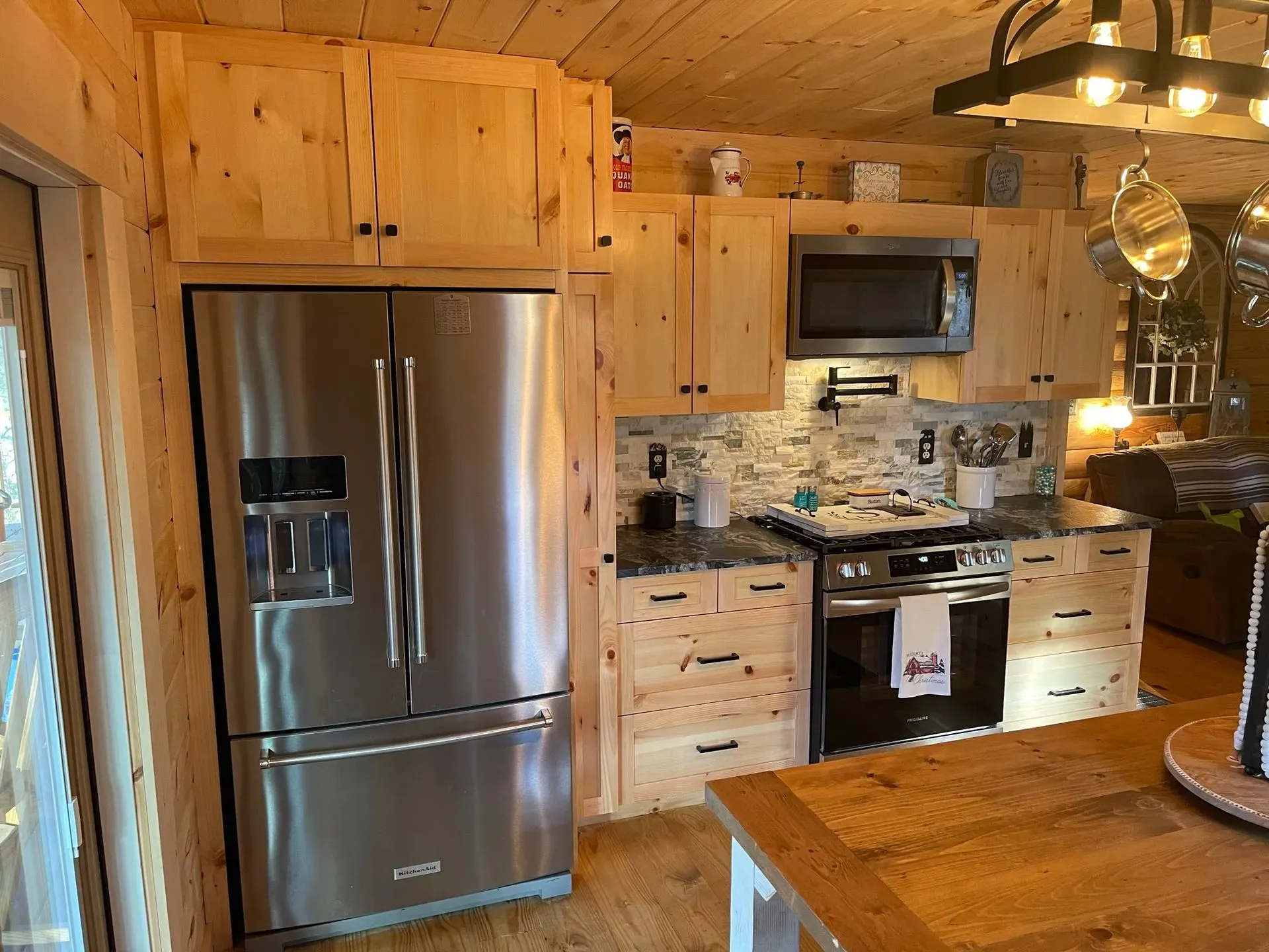 Wood-paneled kitchen with stainless steel fridge, oven, and cabinets beneath warm pendant lighting