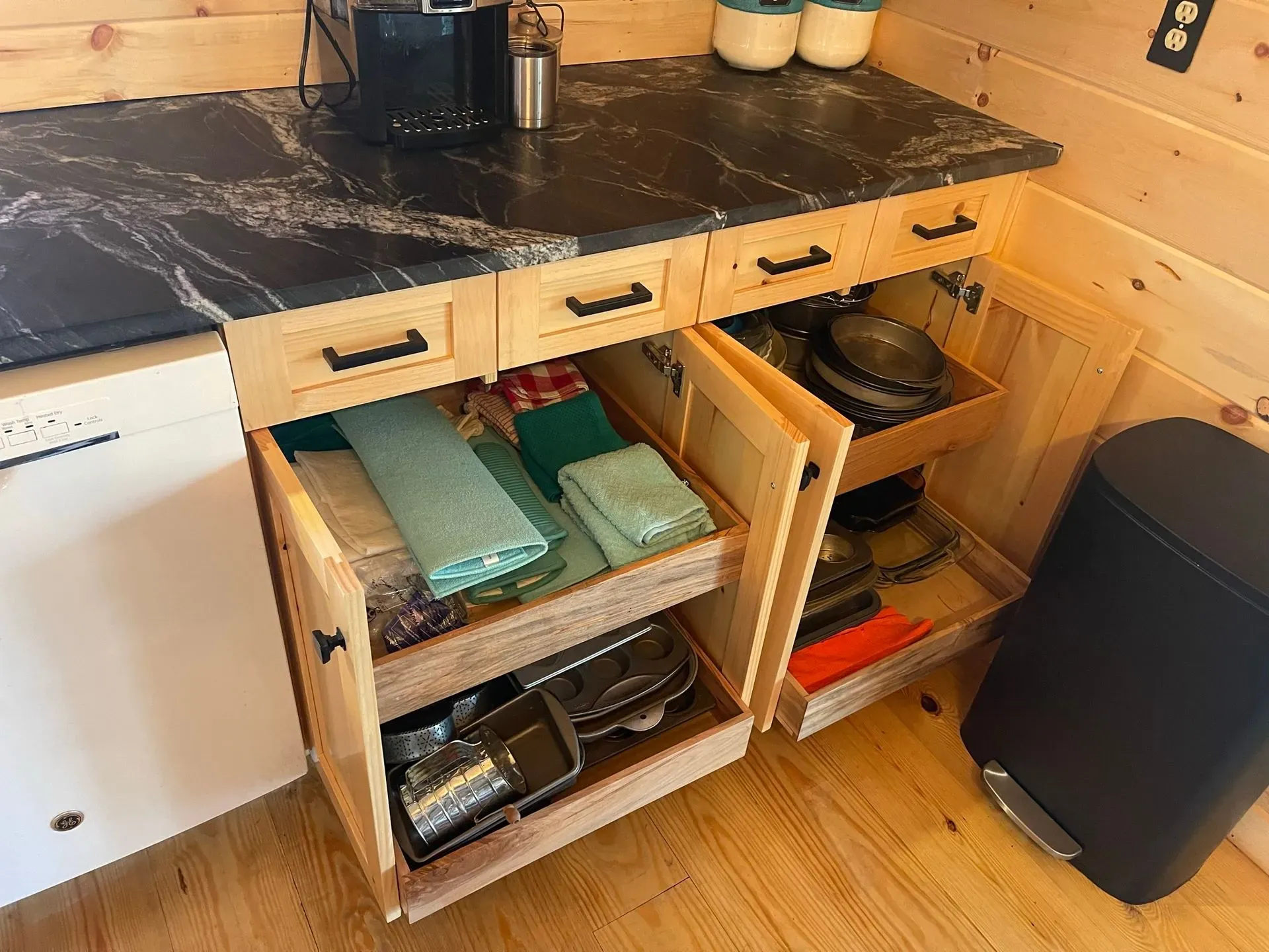 Open kitchen cabinet with organized shelves, drawers, and cookware under a black countertop.