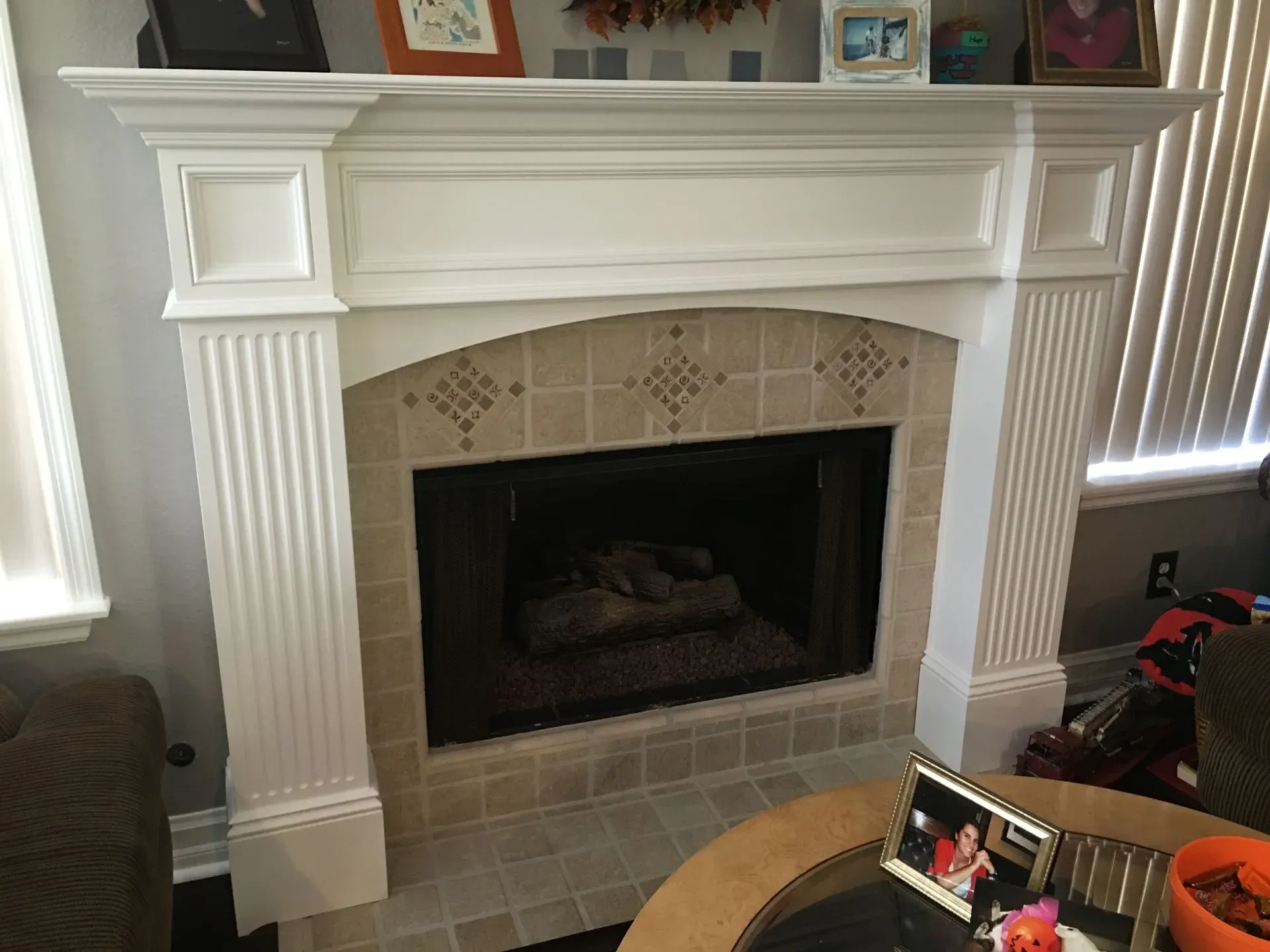 White living room fireplace with mantel, tiled hearth, and decorative trim beside a window with vertical blinds