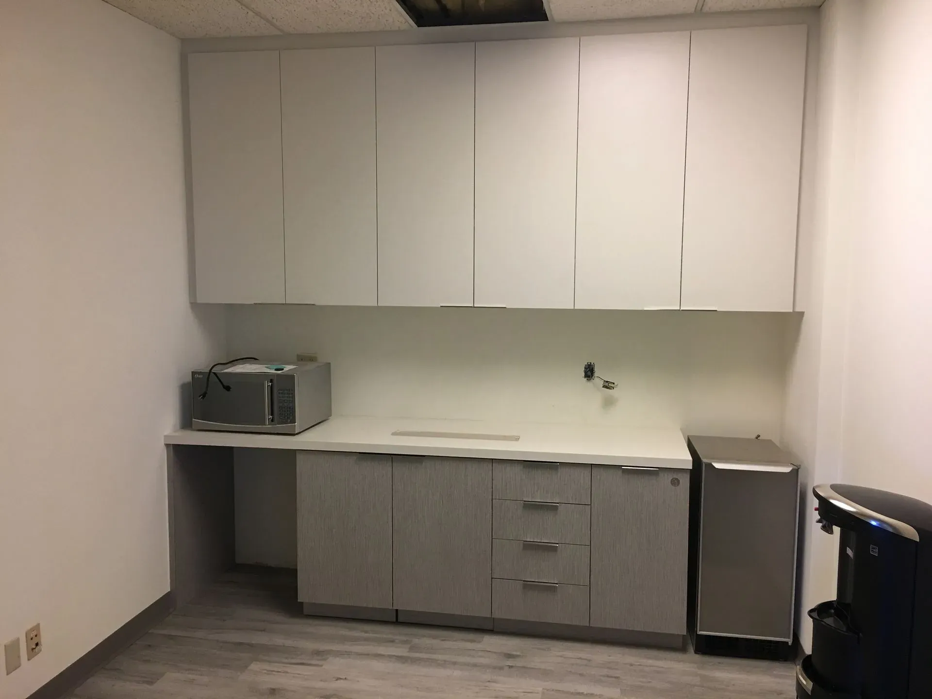 Small break room with white cabinets, gray counter, microwave, mini fridge, and a chair.