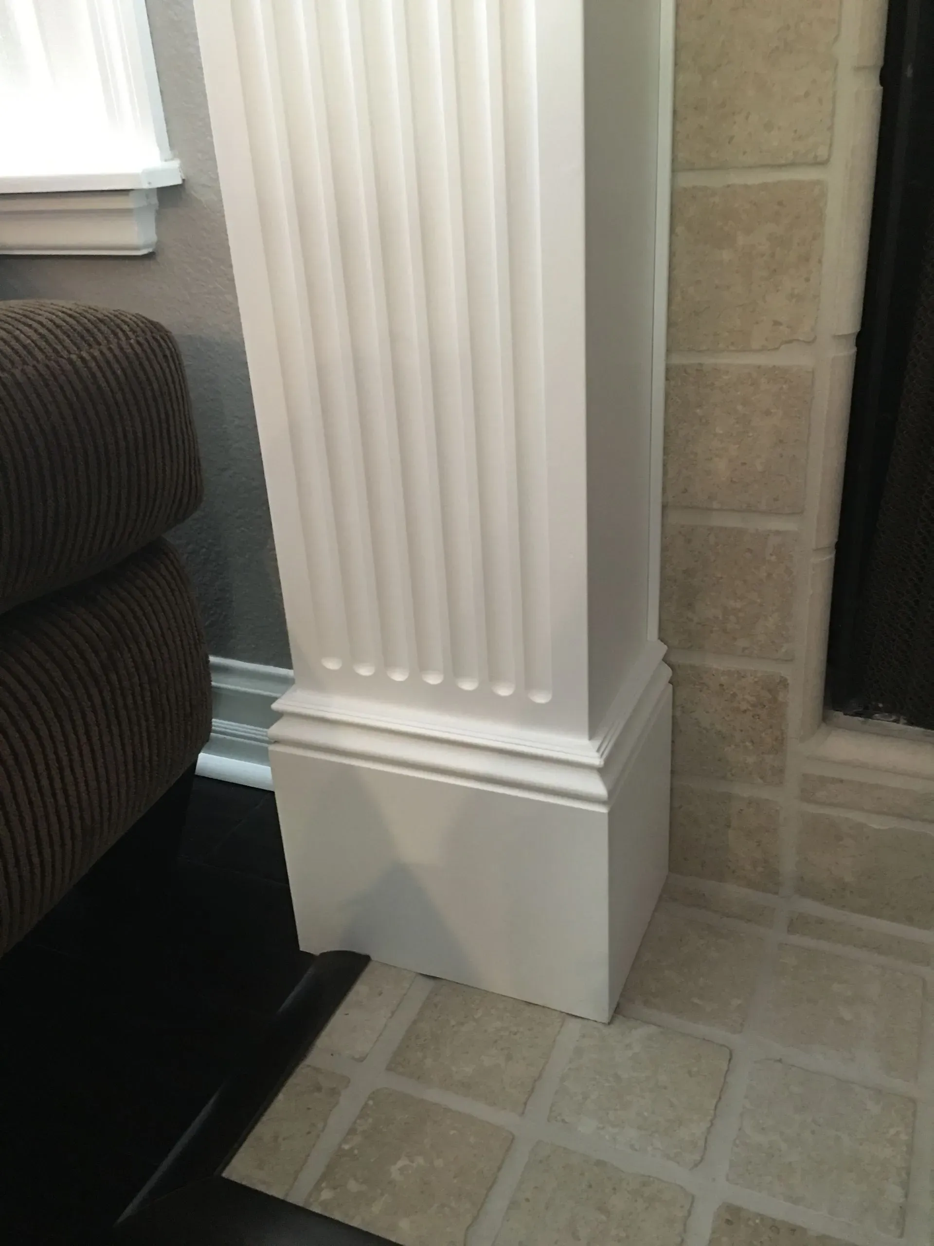 White fluted column base beside a tan tile floor and dark fireplace opening