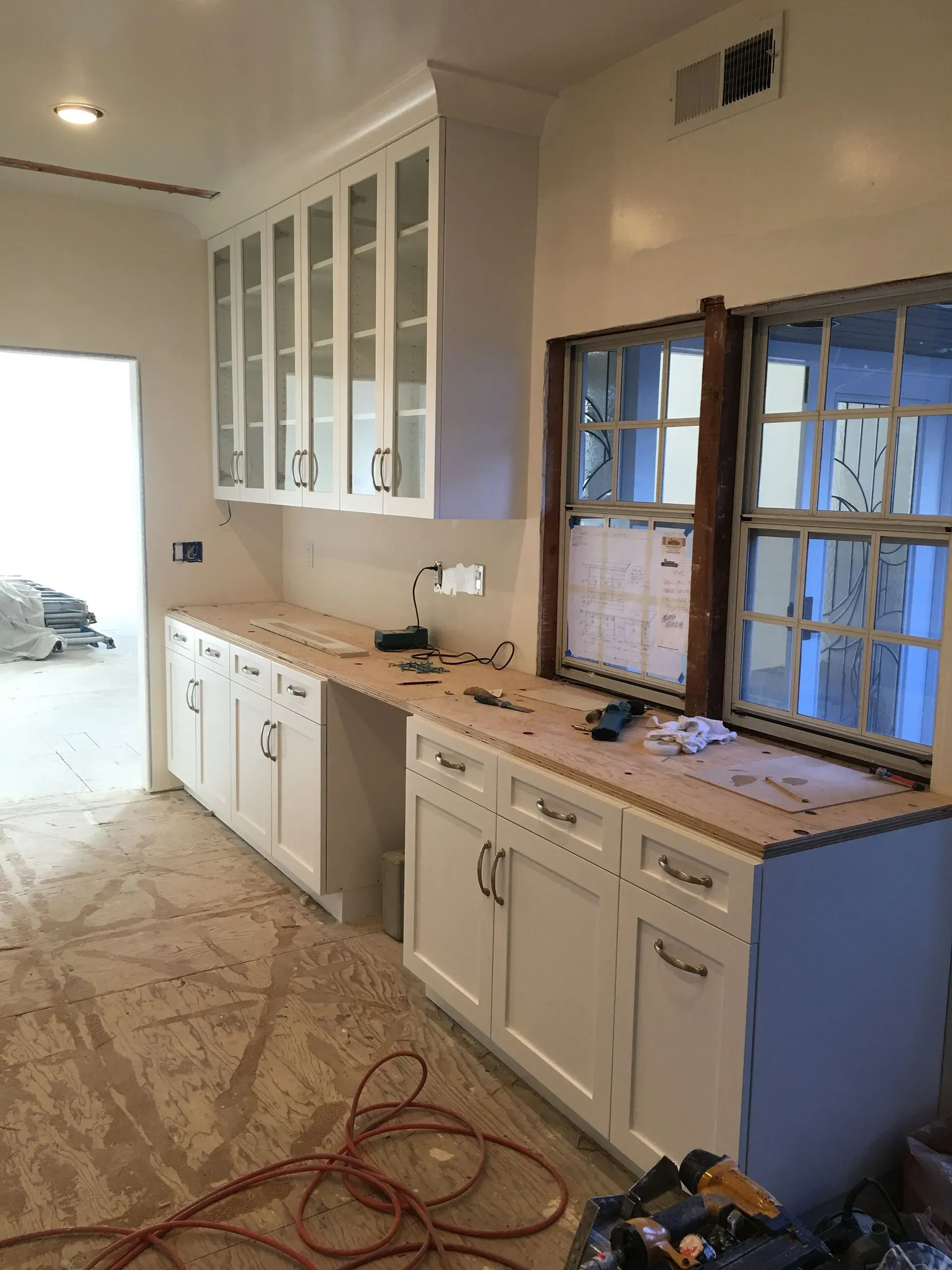 Partially renovated kitchen with white cabinets, exposed wall framing, and tools on the floor