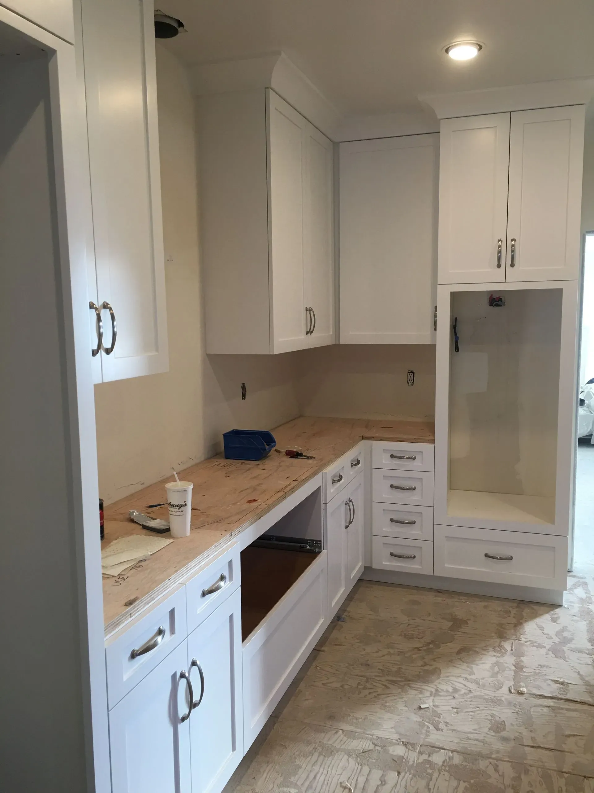 Bright white kitchen with cabinets, beige countertops, built-in oven, and a refrigerator.