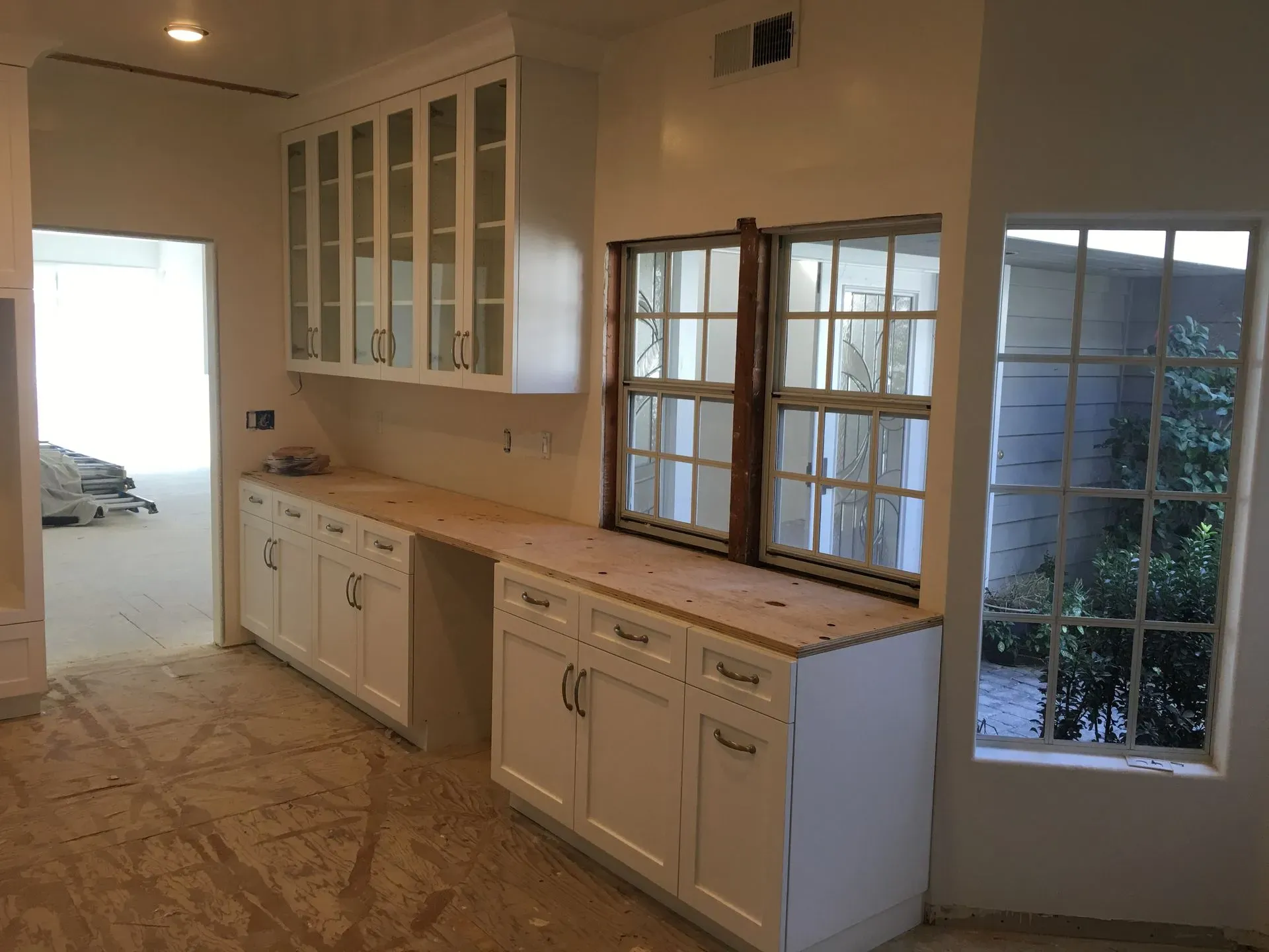 Empty kitchen with white cabinets, beige countertops, and a windowed door leading outside.