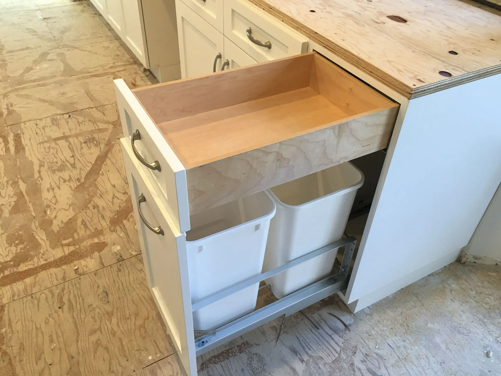 Open kitchen drawer with white trash and recycling bins under a countertop sink area