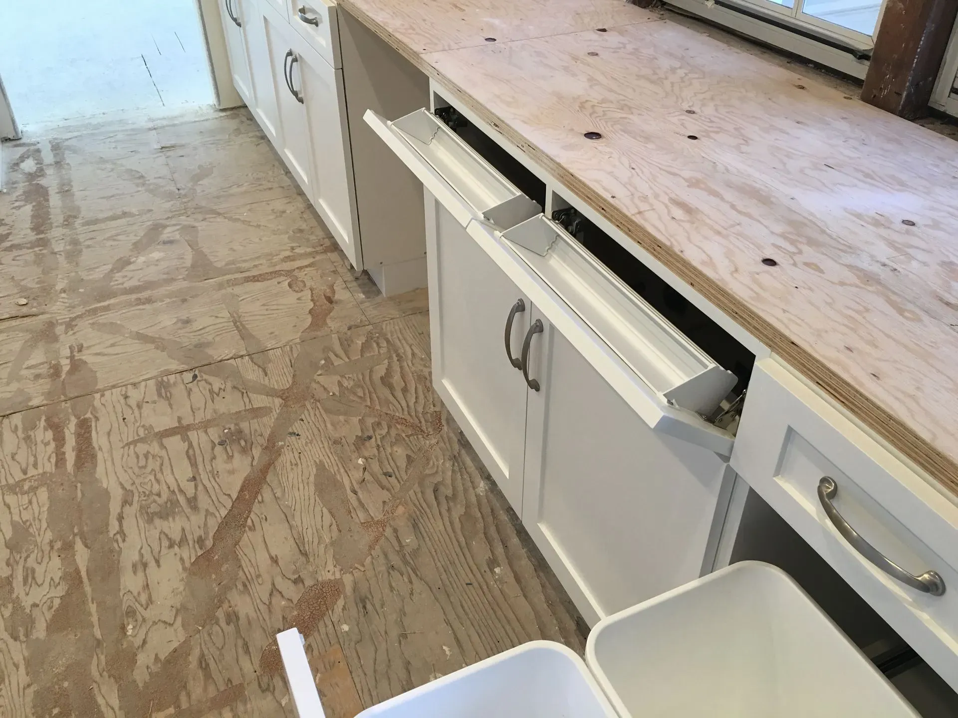 Kitchen floor with damaged white cabinets and detached drawers beside a wooden countertop