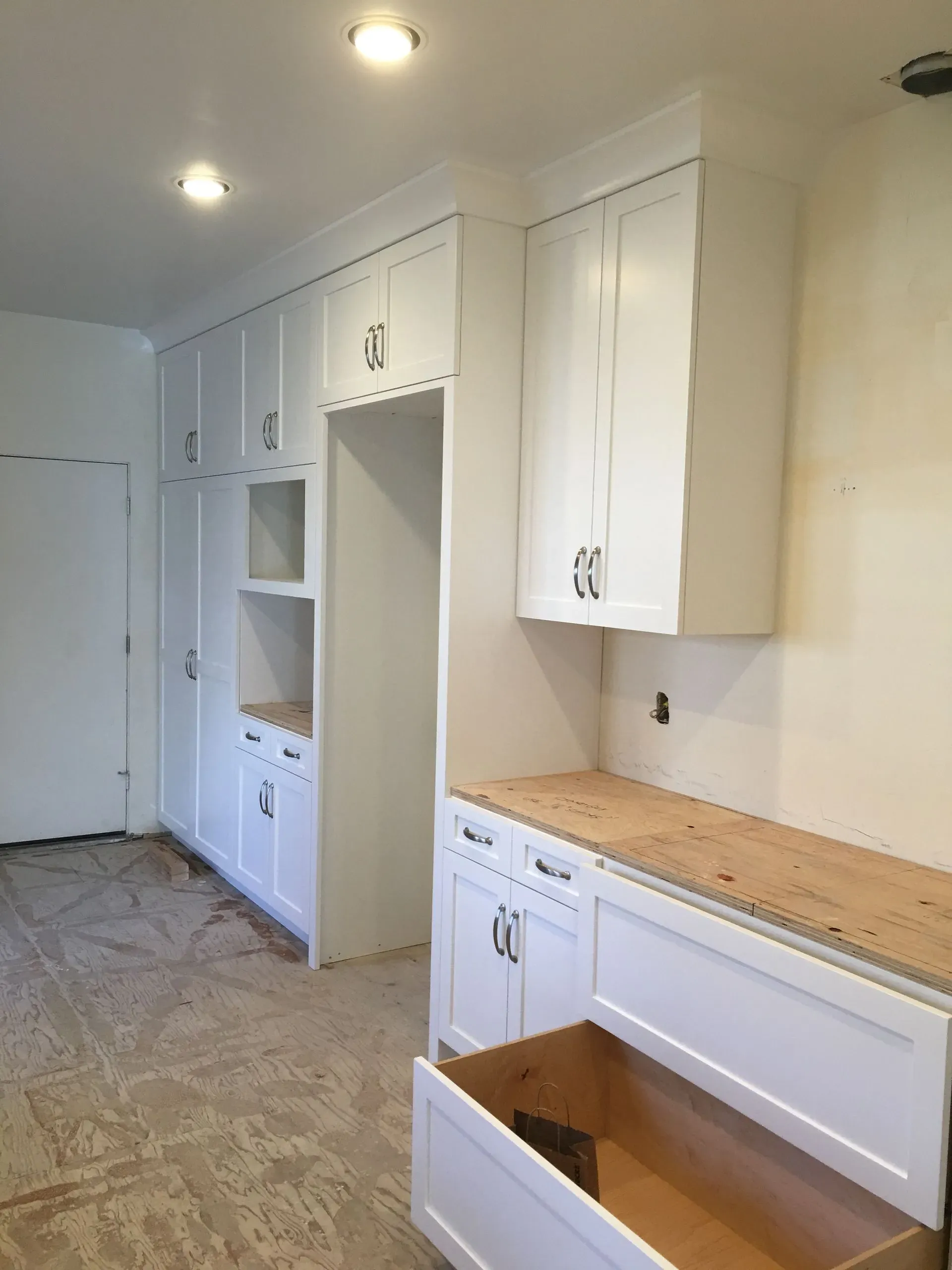 White hallway with built-in cabinets and open drawers, lit by ceiling lights, with a small wood countertop.