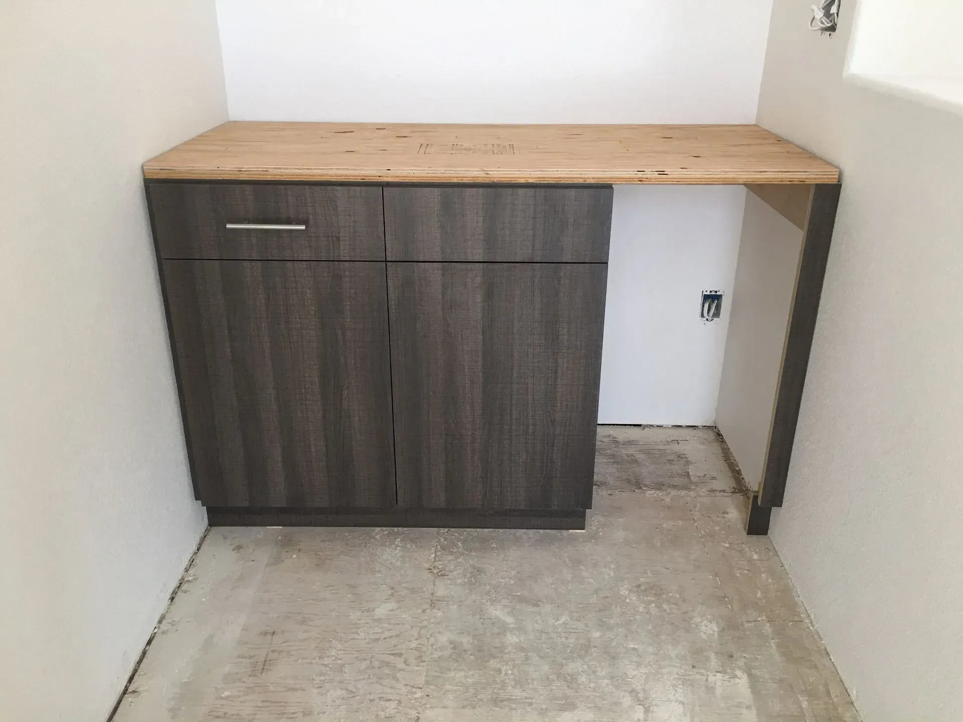 Small kitchen cabinet with wood countertop in an unfinished room with concrete floor