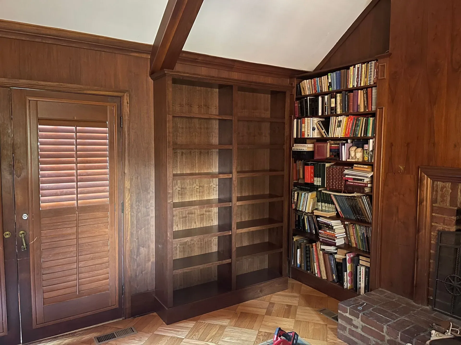 Wood-paneled room with built-in bookshelves, a shuttered window, and a brick fireplace.