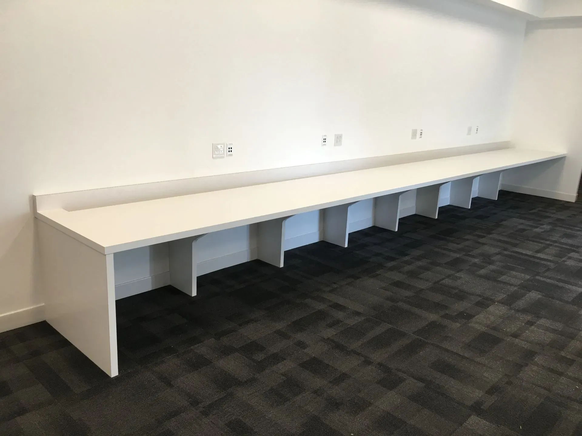 Long white built-in desk with multiple cubbies against a wall in a carpeted office room