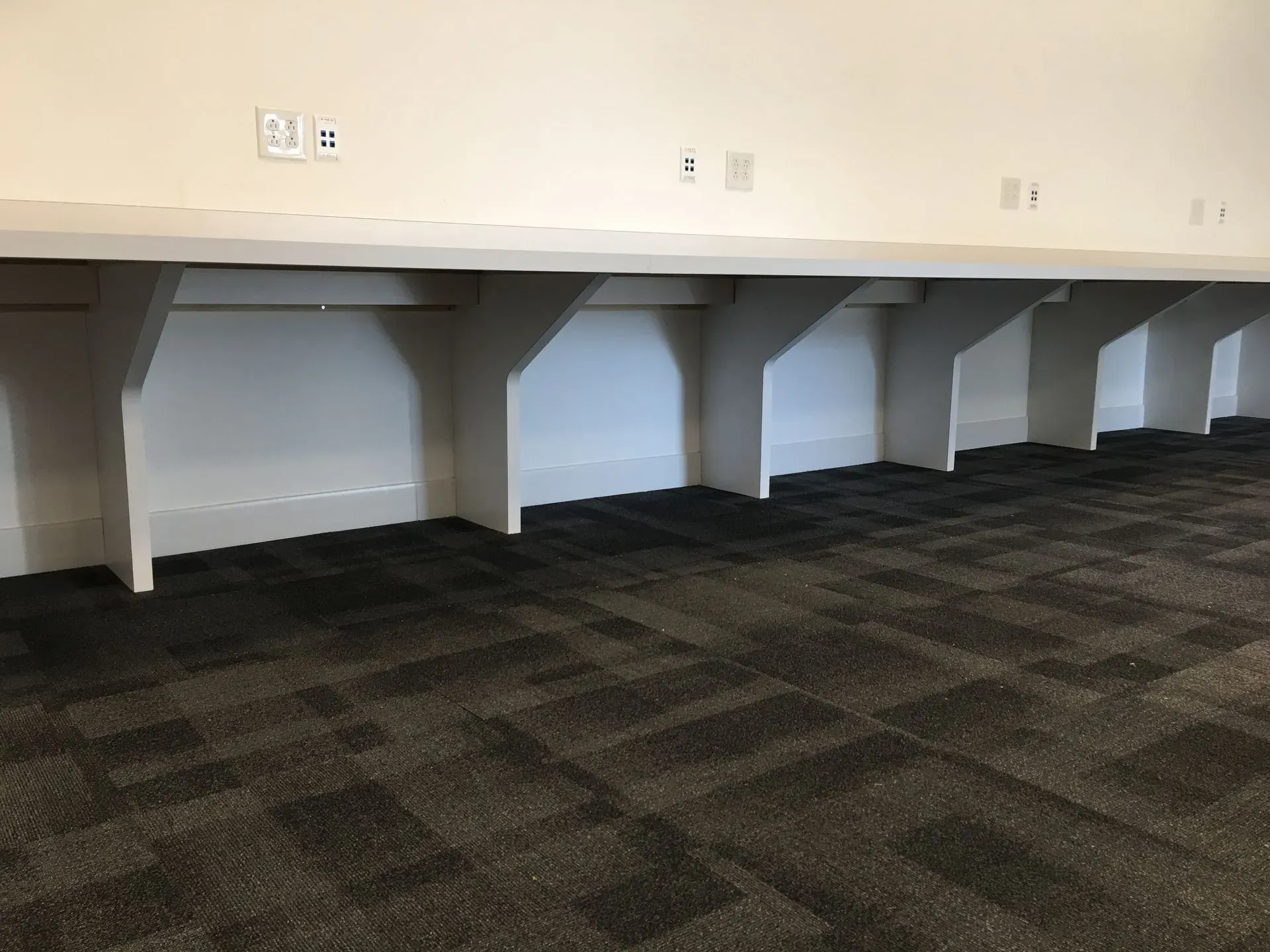 Empty room with built-in white cubicles and dark patterned carpet along a wall