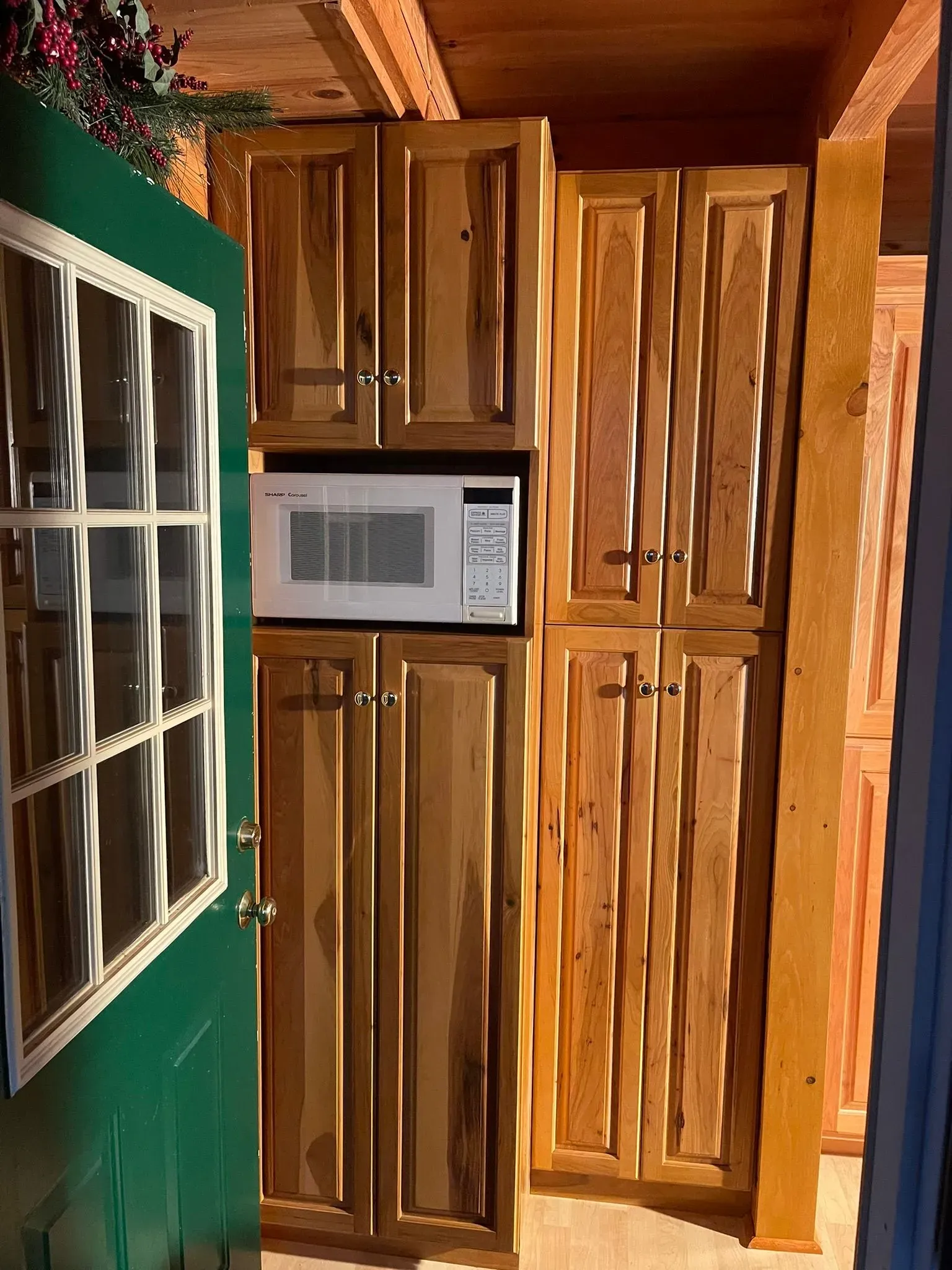 Wooden kitchen cabinets with a built-in microwave beside a green door and window.