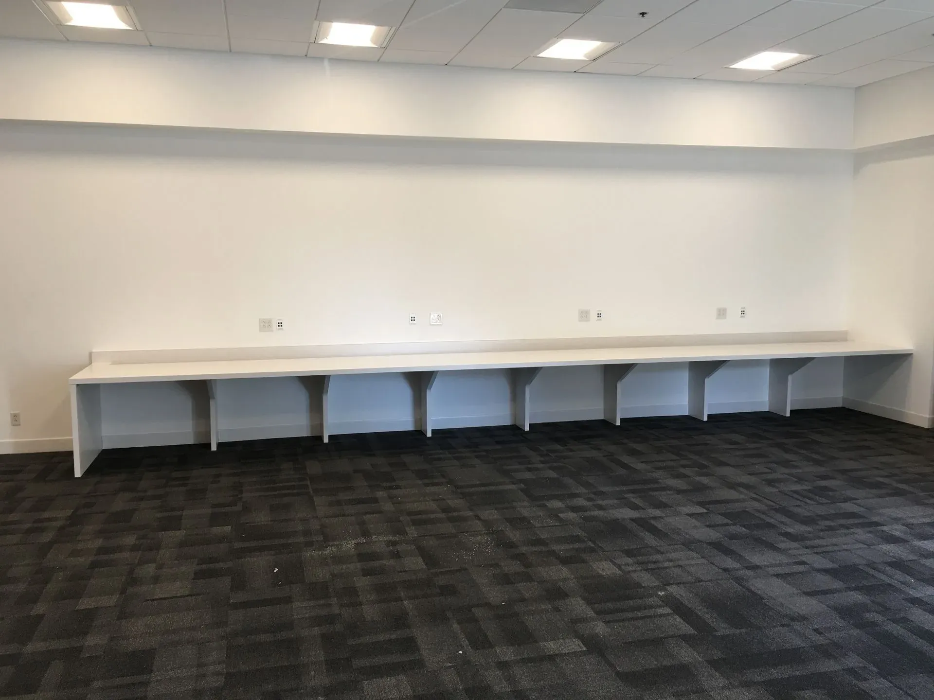 Empty office room with white wall-mounted desks and dark carpet flooring