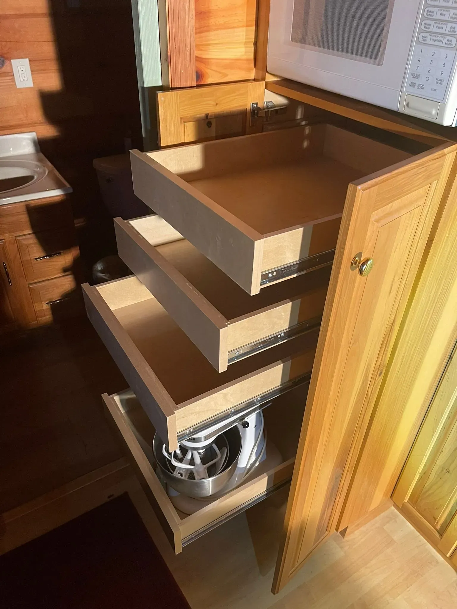 Open wooden drawers in a kitchen cabinet, with a wire basket and a partially visible appliance below.