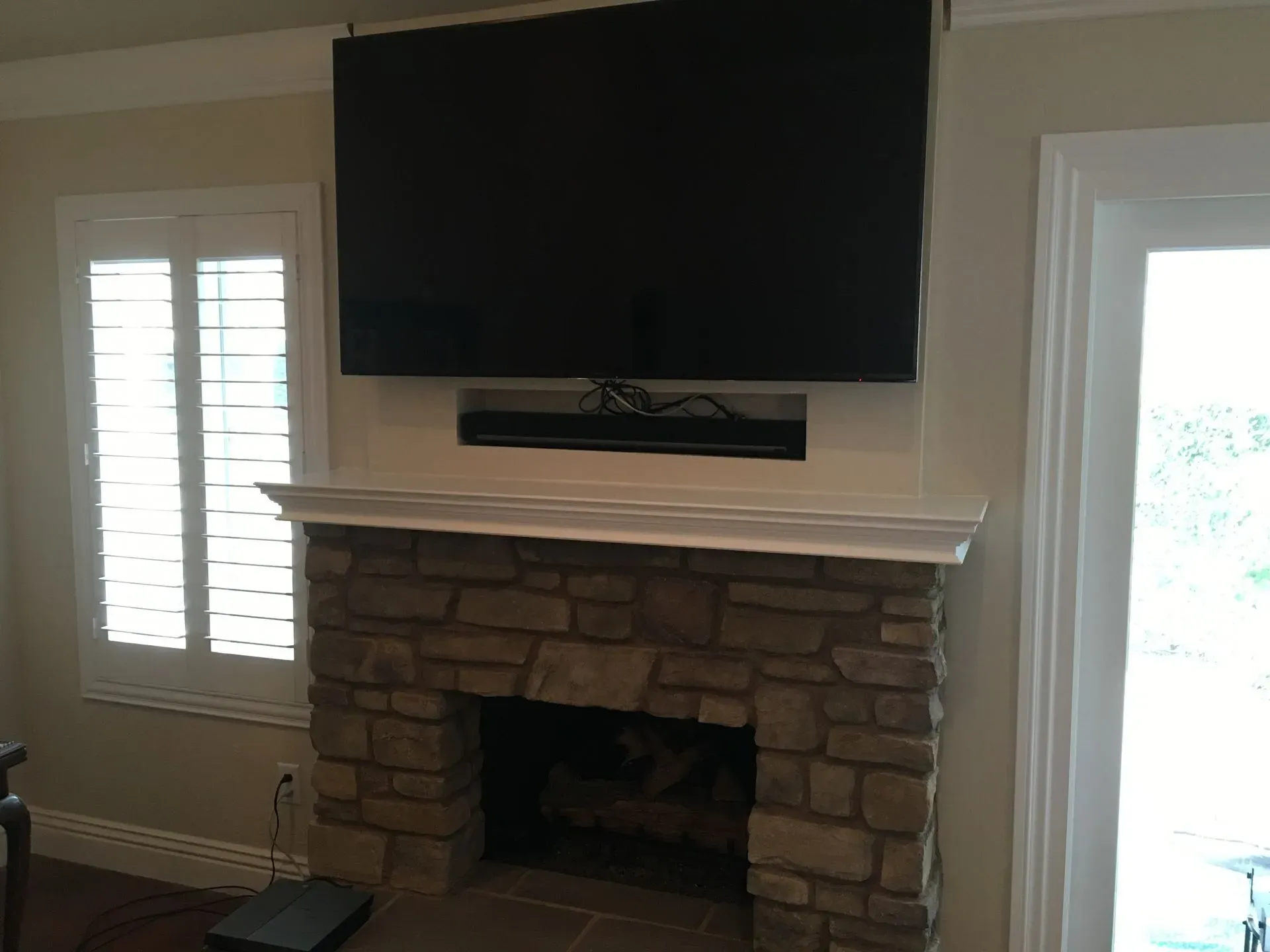 Living room fireplace with mounted TV, stone surround, white mantel, and bright windows on both sides