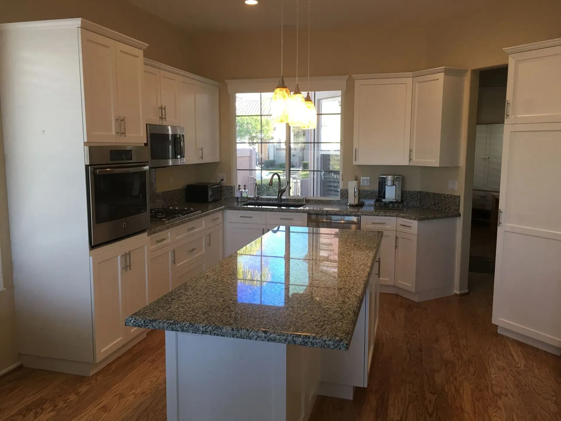 Bright modern kitchen with white cabinets, granite island, hardwood floors, and a window over the sink.