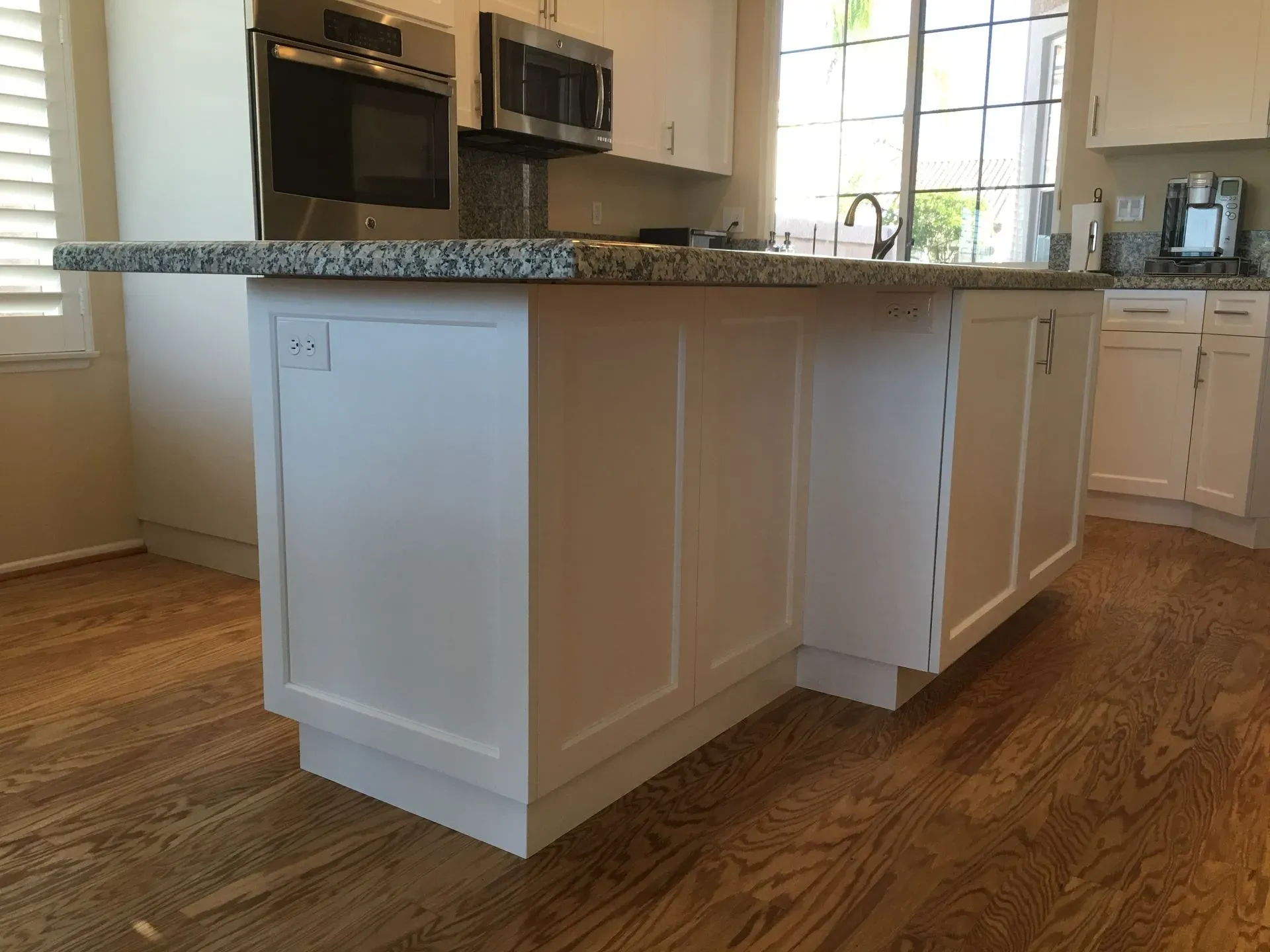 Modern kitchen with a large white island, wood floors, and stainless steel appliances