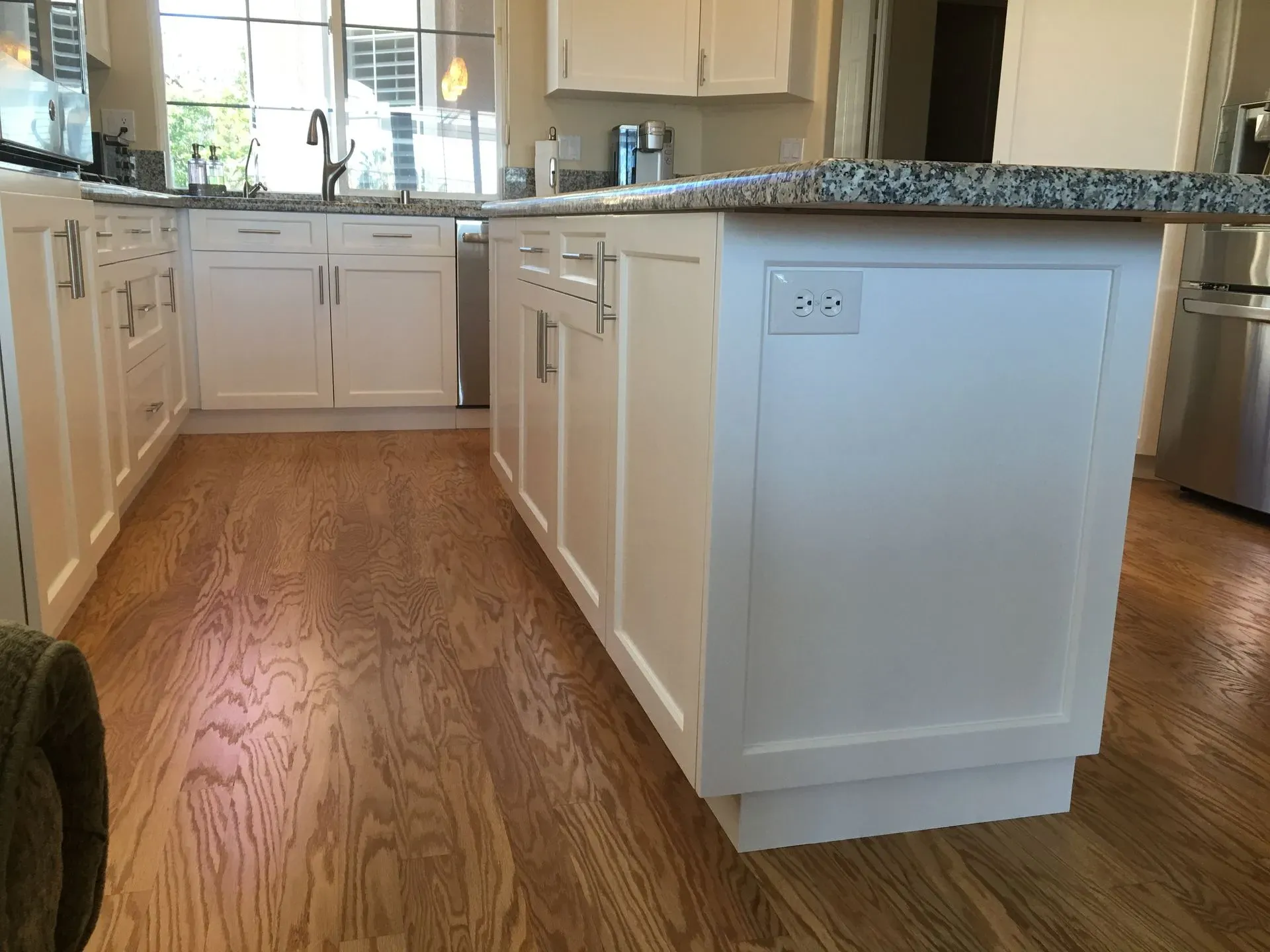 Bright kitchen with white cabinets, granite counters, and wood floors, viewed from the island area