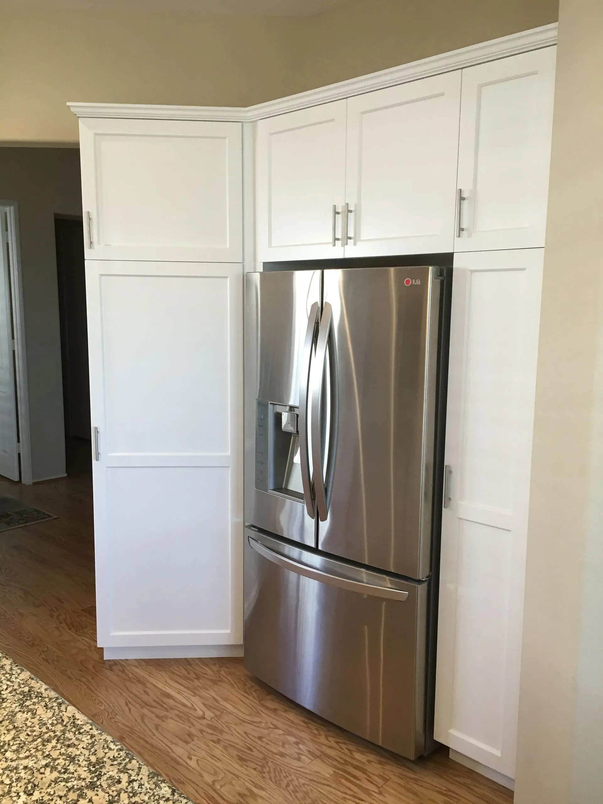 White kitchen cabinets with a stainless steel refrigerator beside a doorway and hardwood floor.