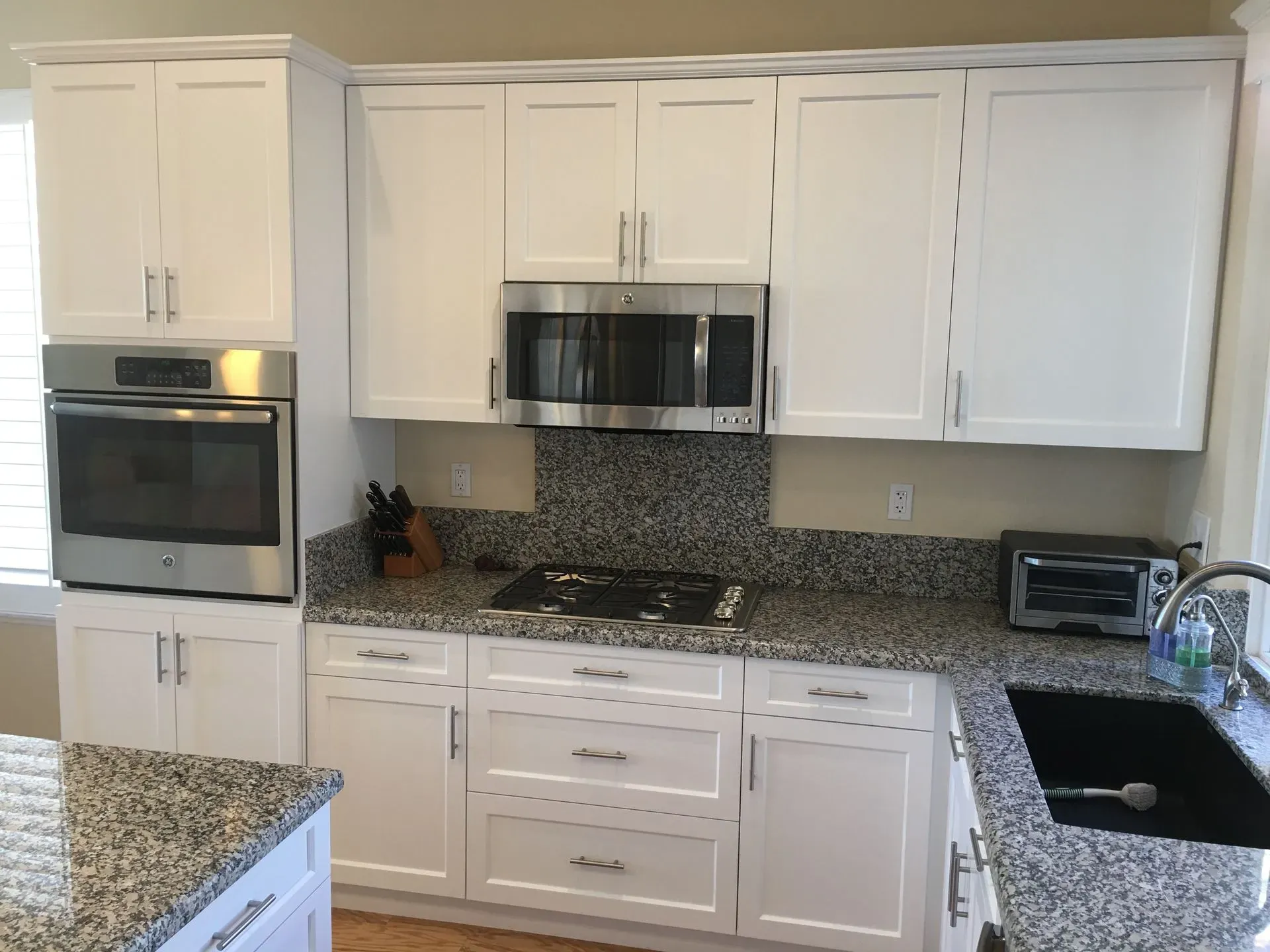 Modern white kitchen with granite counters, stainless appliances, and black stove top