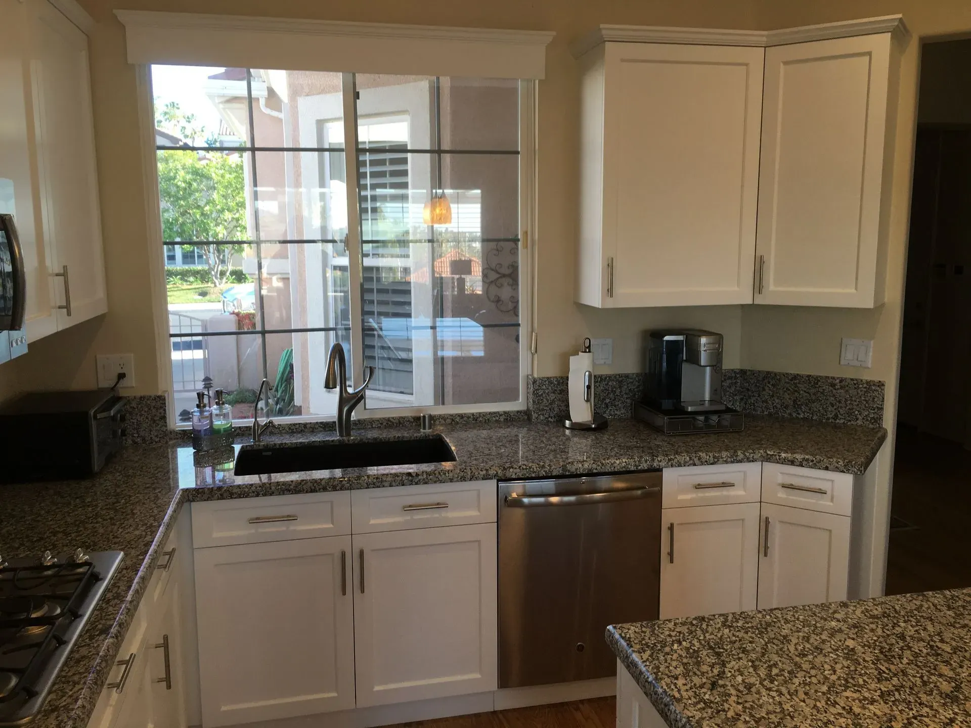 Bright kitchen with white cabinets, granite counters, stainless dishwasher, and a sink below a window