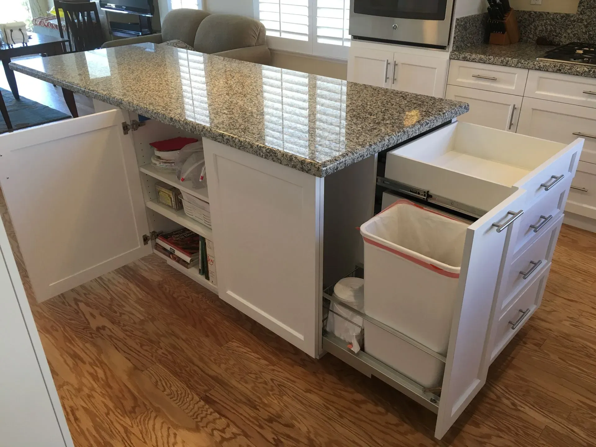 Kitchen island with granite countertop and pull-out storage drawers, one cabinet open showing shelves and bins.
