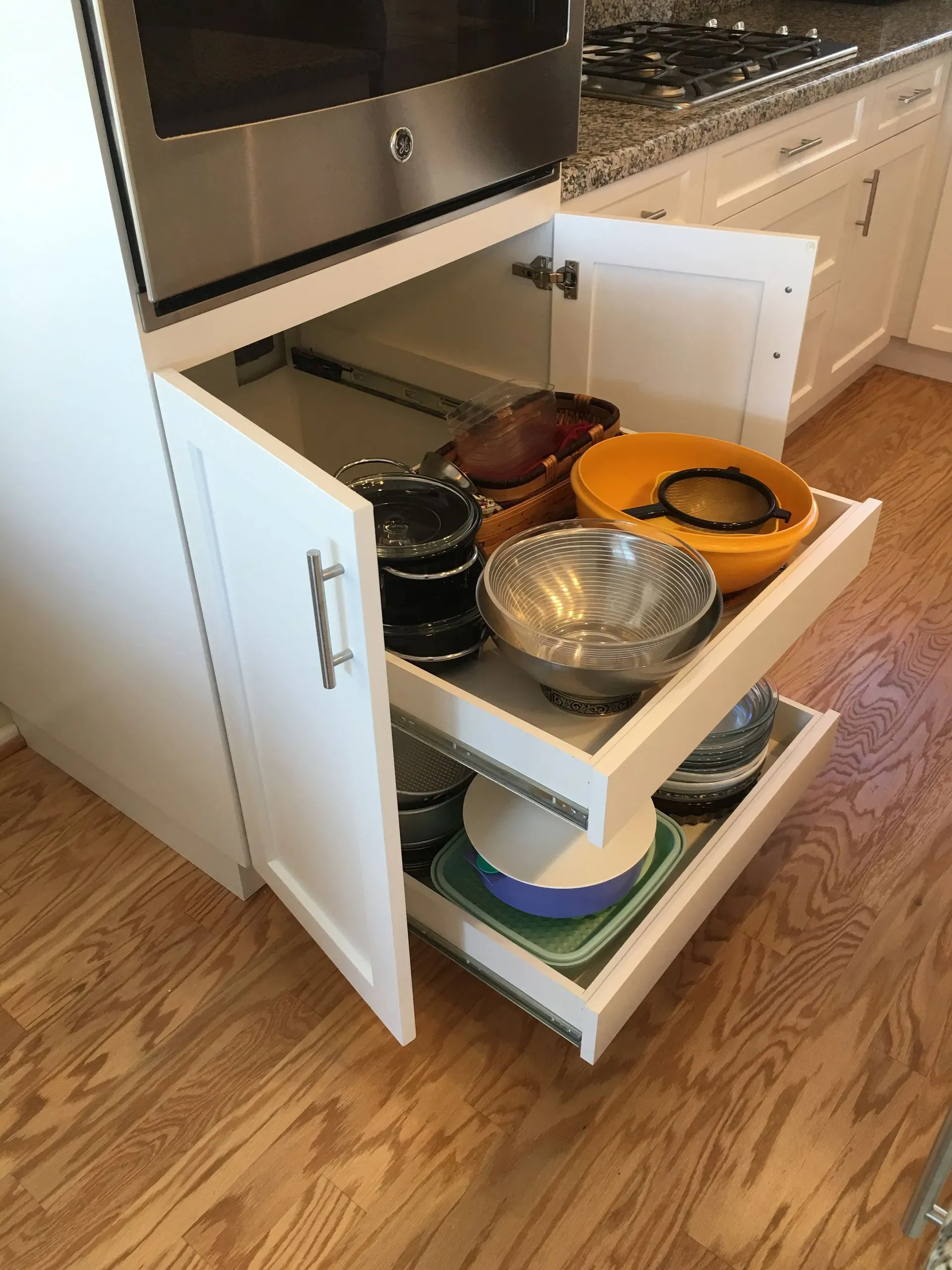 Open kitchen cabinet with pull-out shelves holding bowls, plates, and cookware on a wood floor.