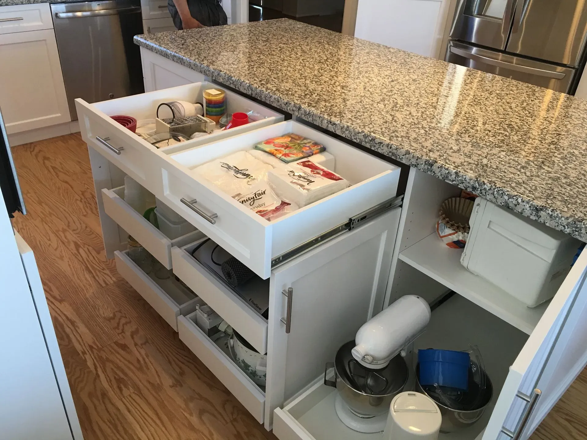 Kitchen pull-out pantry drawers with food and cookware organized beside a granite counter.