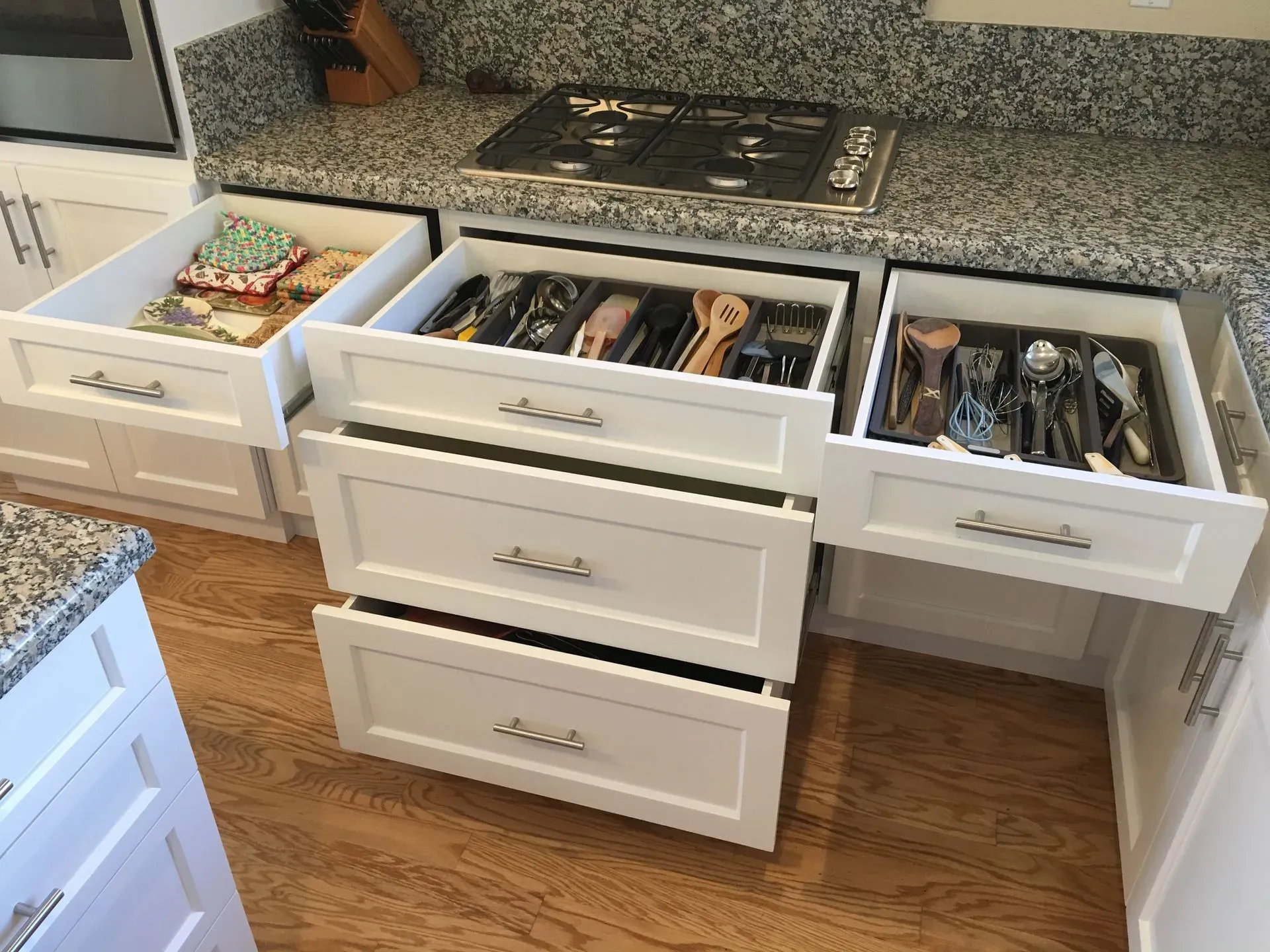 White kitchen drawers open to reveal organized silverware and utensils under a granite countertop.