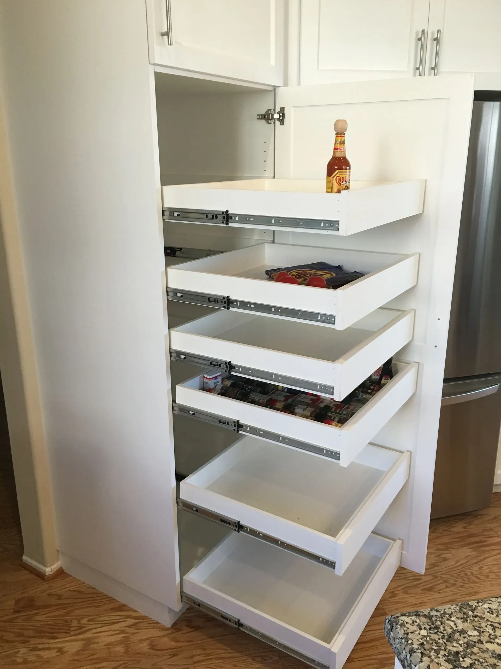 Pull-out pantry drawer with white shelves holding spices and kitchen items in a white cabinet