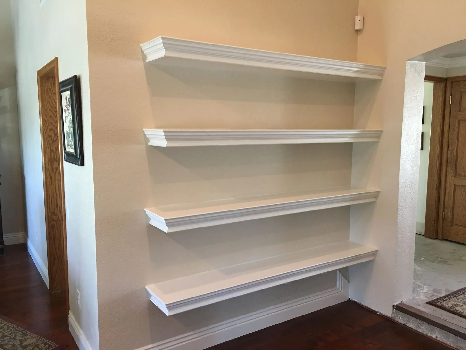 White wall-mounted shelves on a beige hallway wall in a home interior.