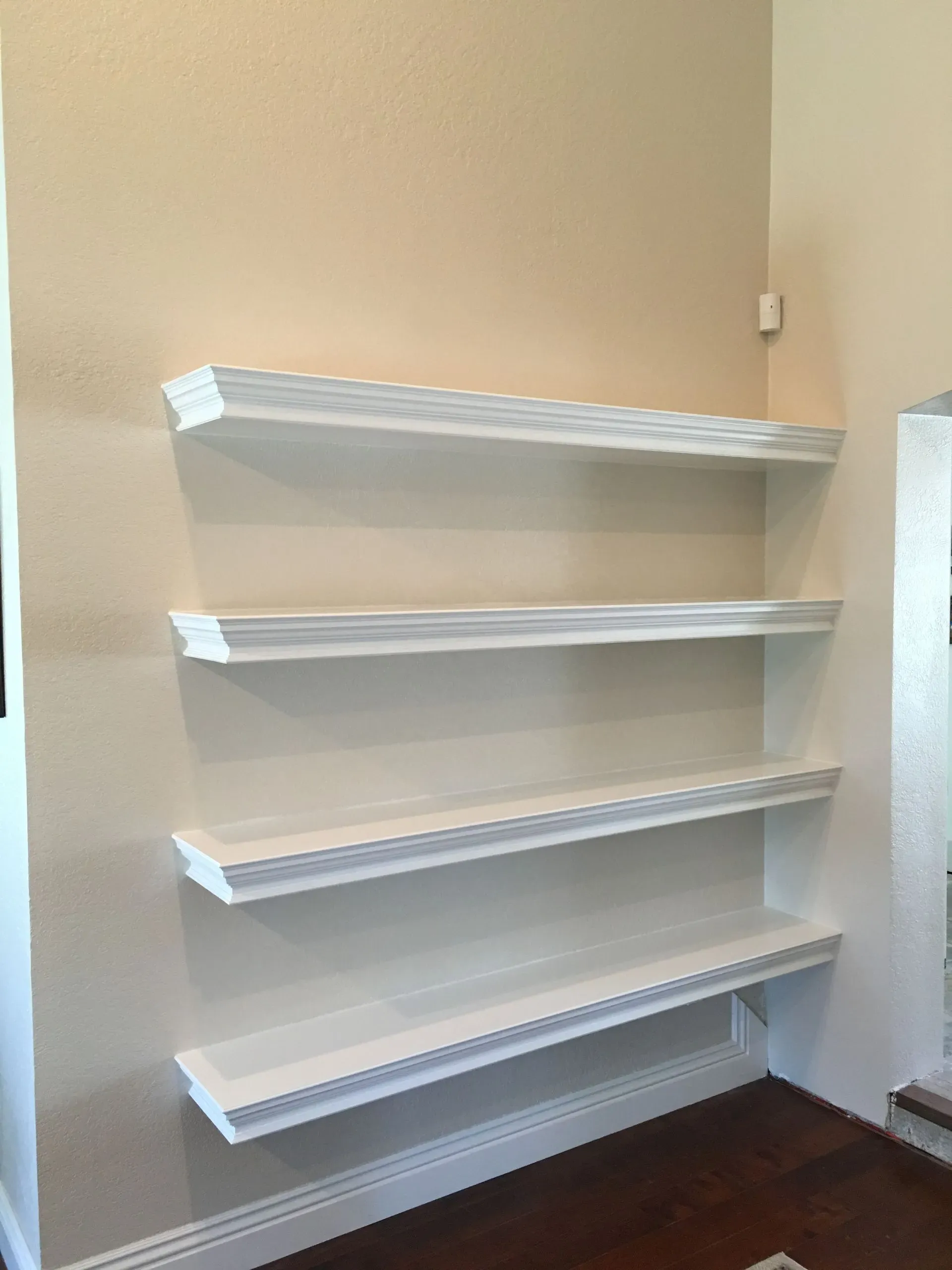 White wall-mounted shelves in a beige room above dark wood flooring.