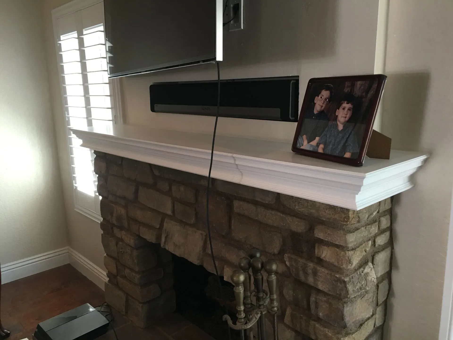Living room fireplace with a stone surround, white mantel, TV, and framed family photo