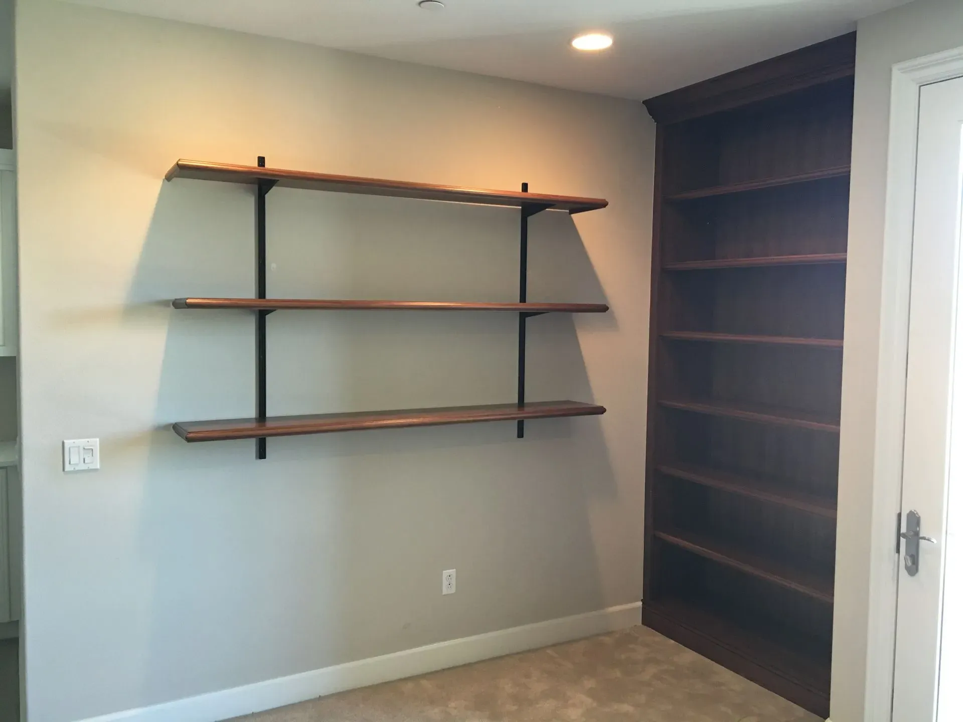 Built-in shelving and wall-mounted shelves in a small empty room with light gray walls and wood trim
