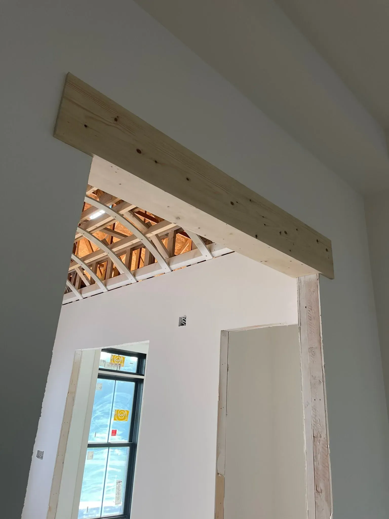 Unfinished interior doorway with exposed ceiling beams and white walls; ladder visible through a side opening.