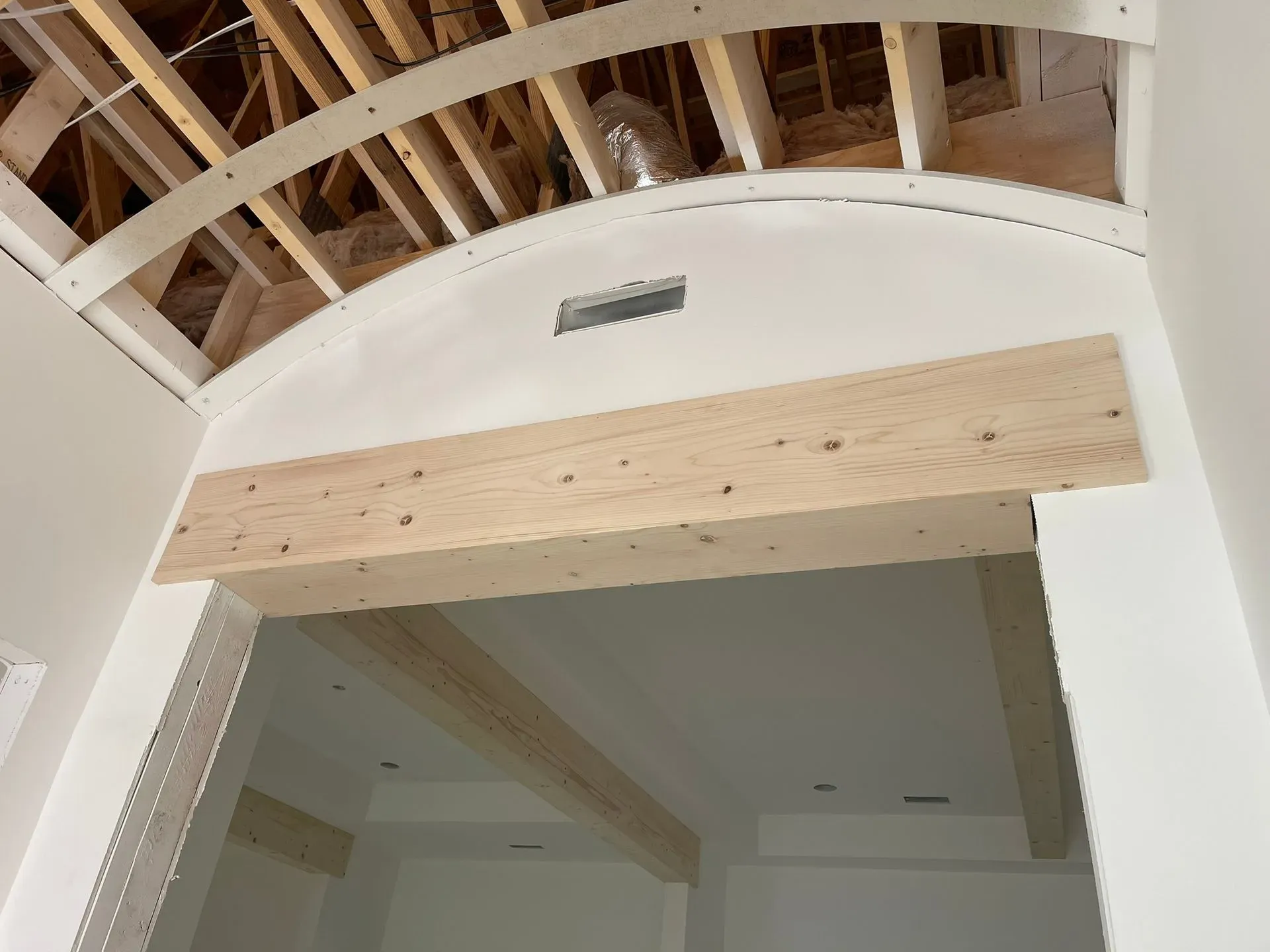 Interior doorway with exposed wooden beams and a light wood header under a curved white ceiling