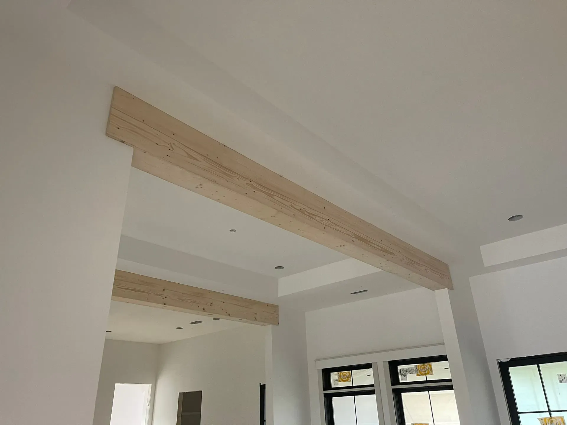 Interior room with exposed wooden ceiling beams and large windows in a bright, unfinished space
