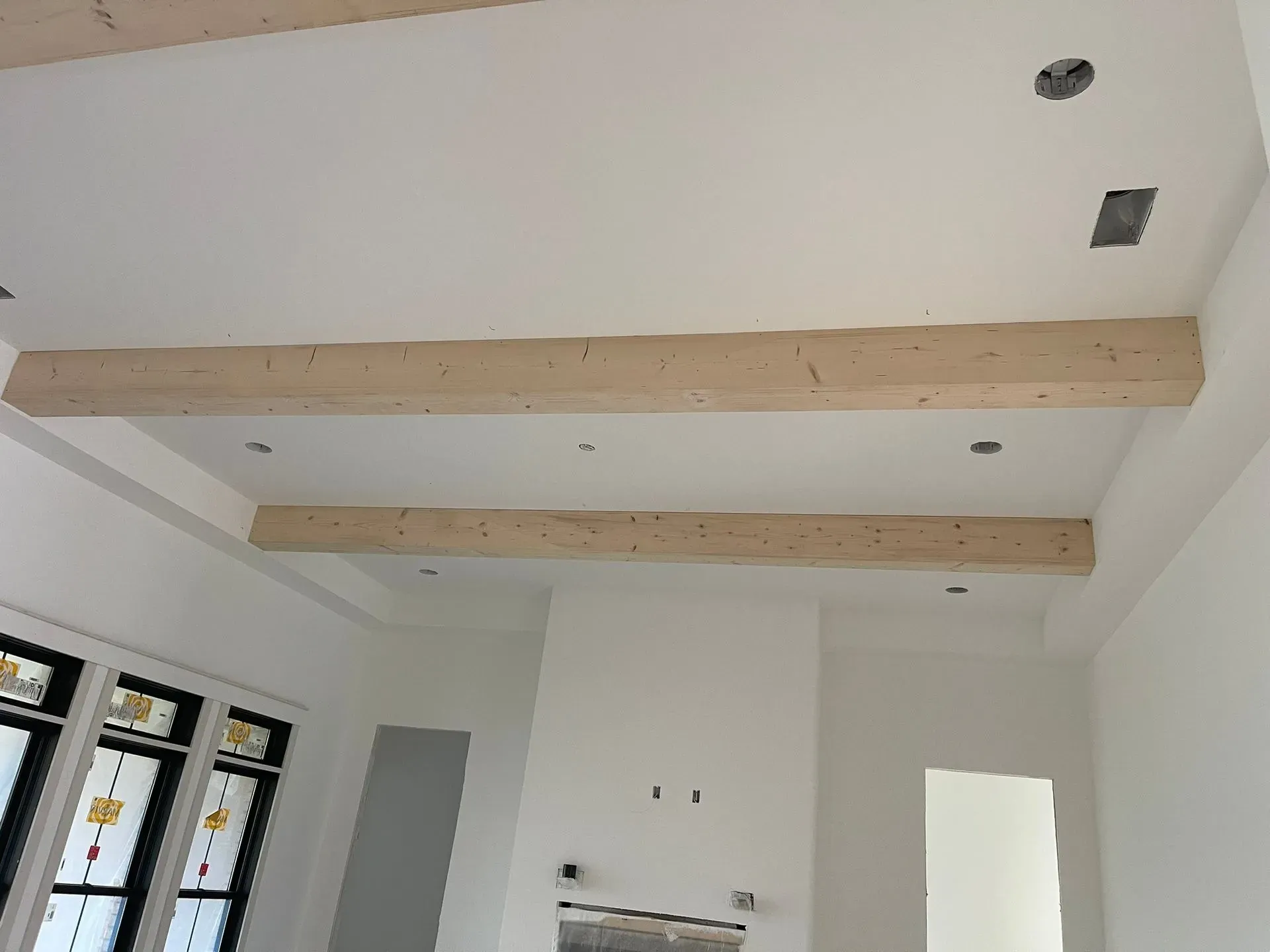 Unfinished room with white walls, exposed wood ceiling beams, and open doorway and windows.
