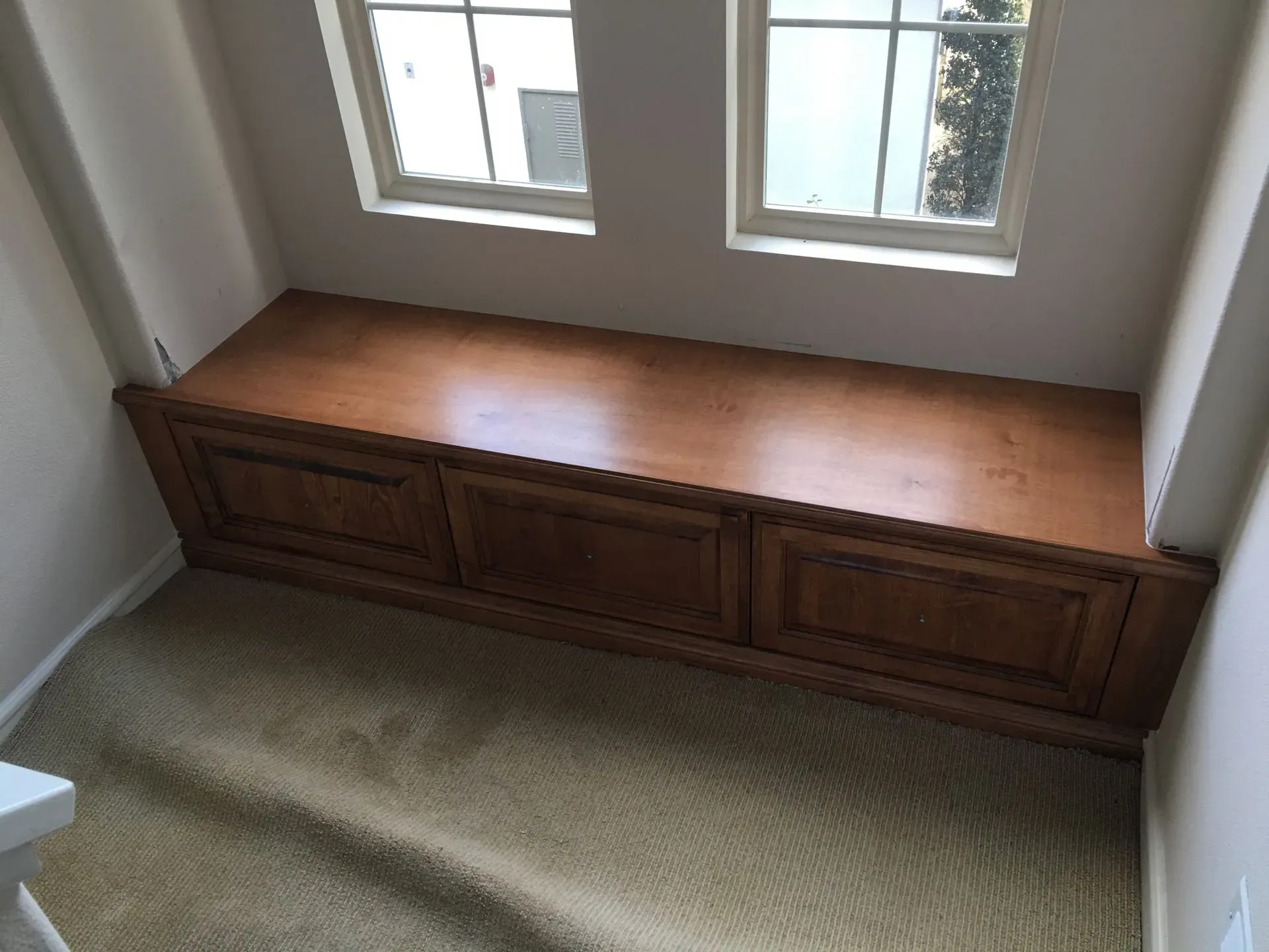 Built-in wooden bench below a window in a carpeted room