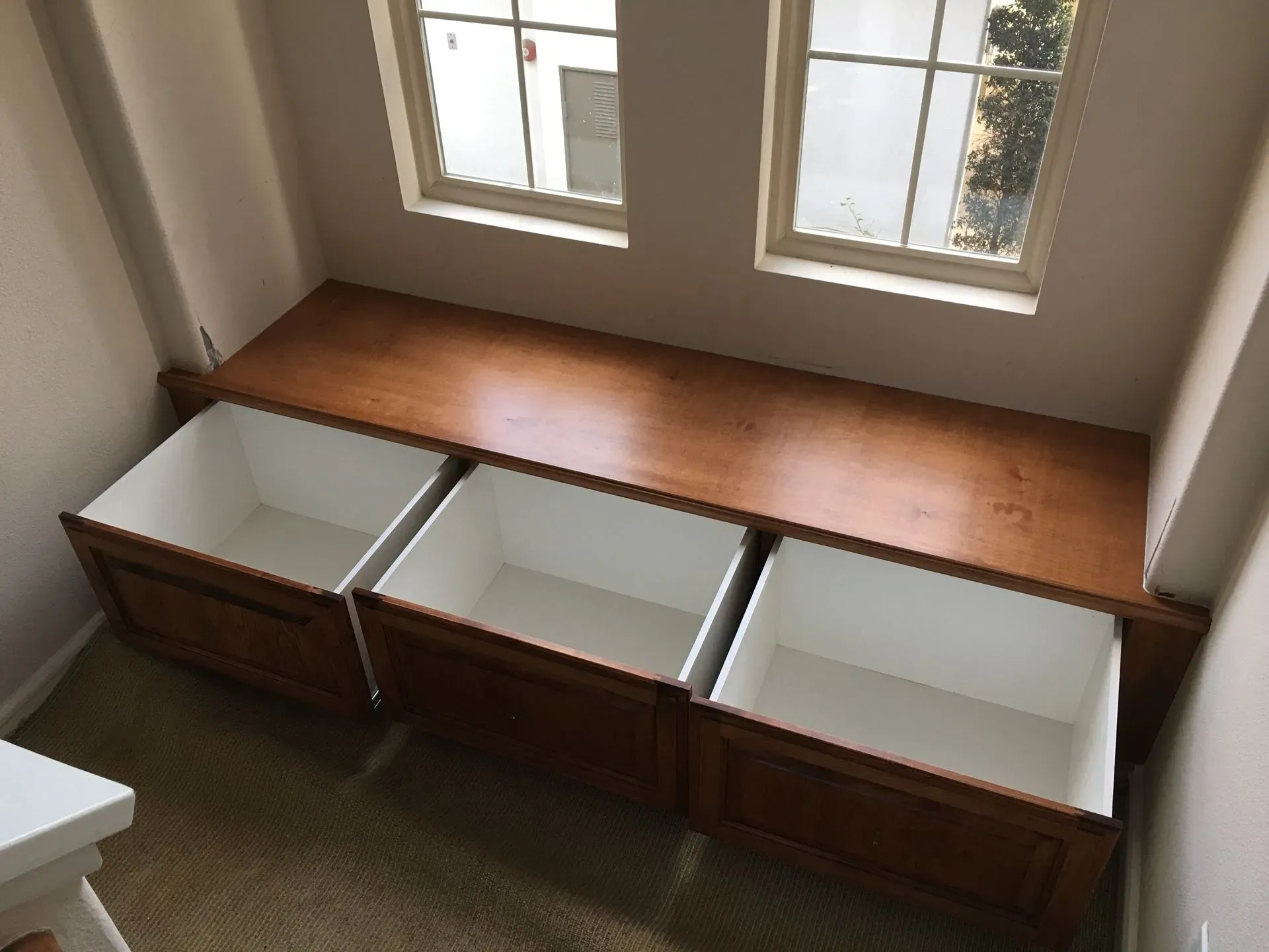 Built-in window bench with open storage bins beneath a wooden top in a bright room